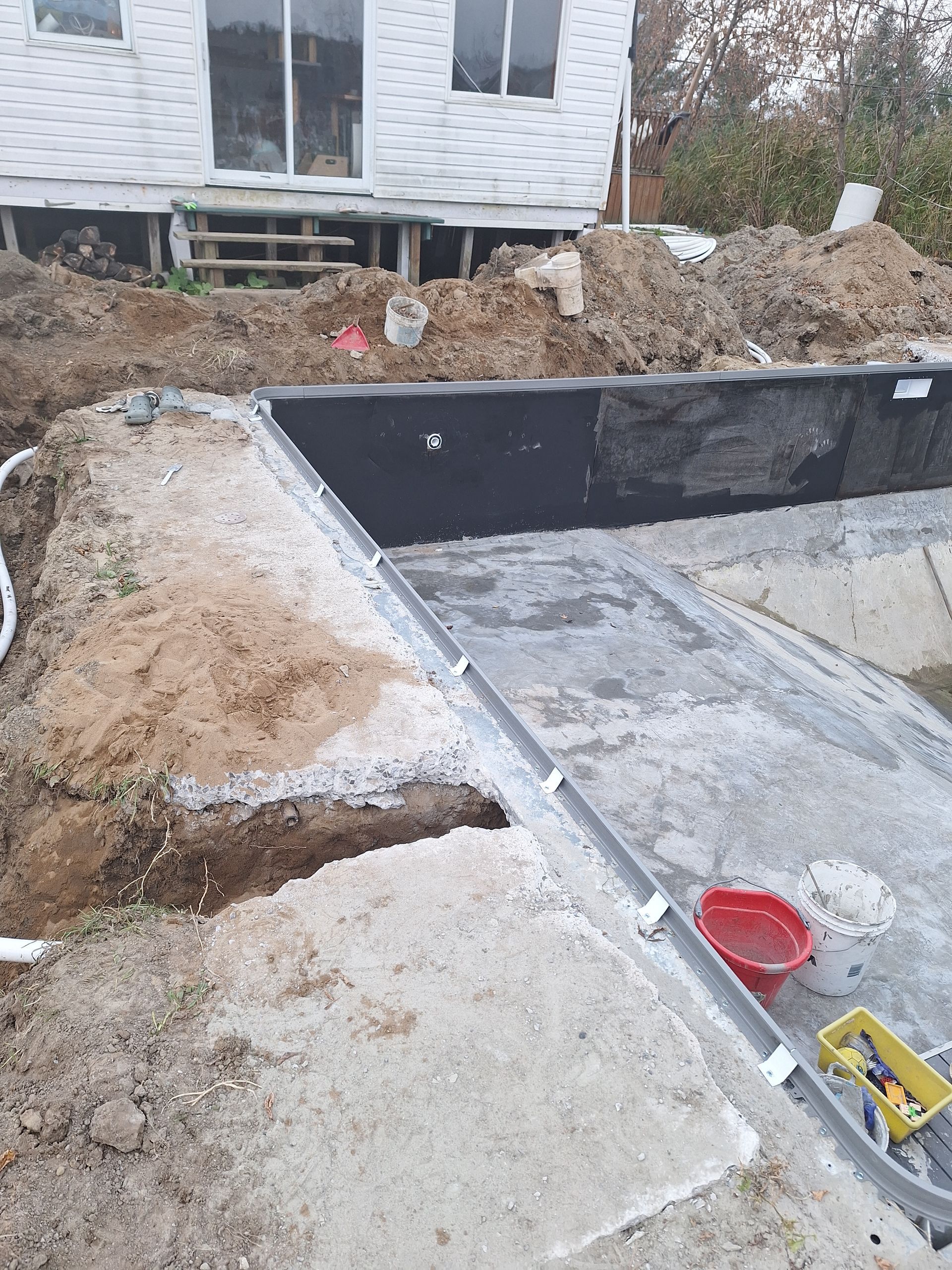 Un chantier de construction résidentielle montrant un angle de fondation en béton avec étanchéité noire, gravier et terre meuble.