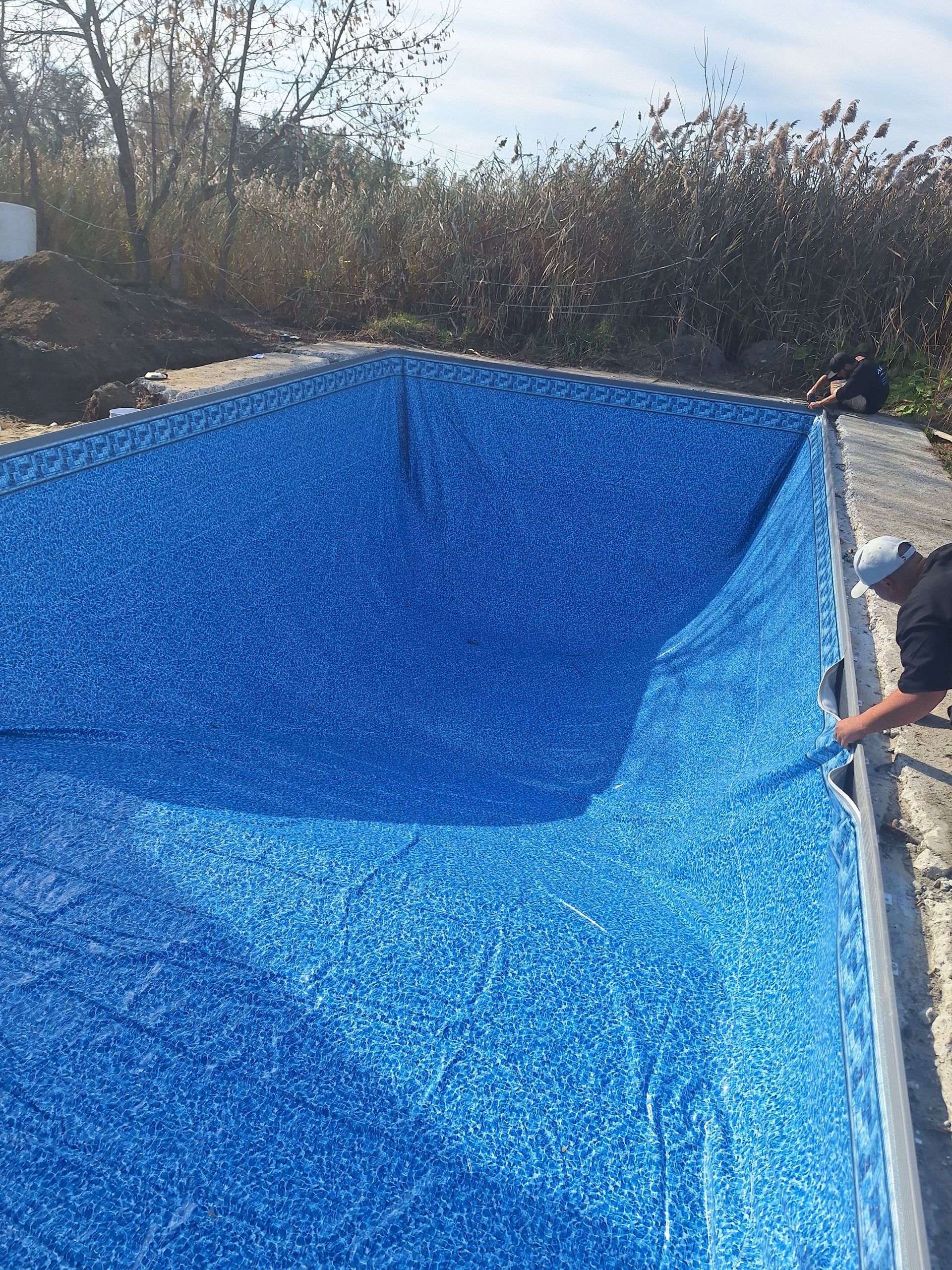 Une personne installe un nouveau revêtement en vinyle bleu à motifs dans une piscine extérieure rectangulaire.