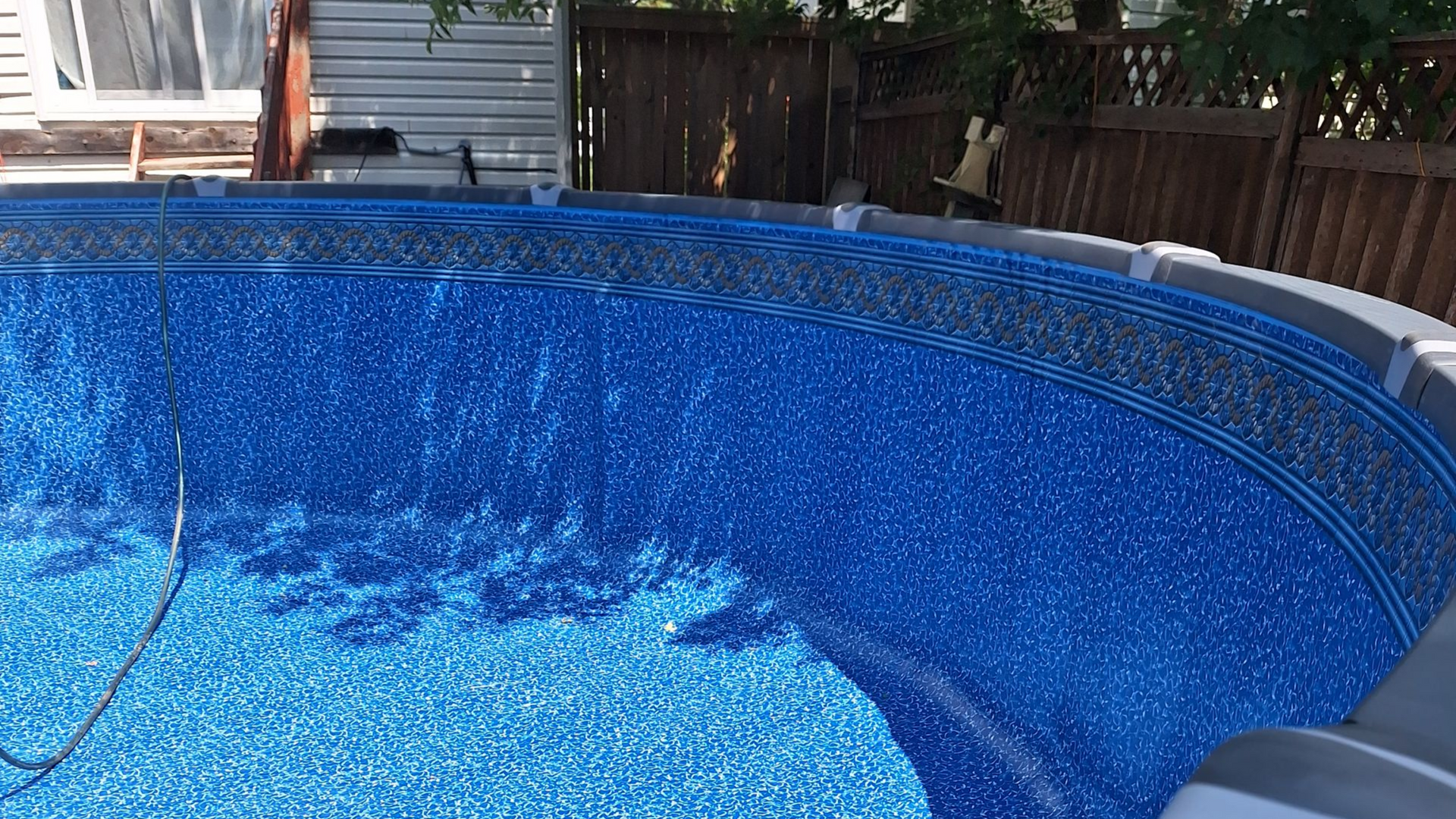 Gros plan sur le revêtement en vinyle bleu à motifs d'une piscine hors sol, sous un soleil éclatant.