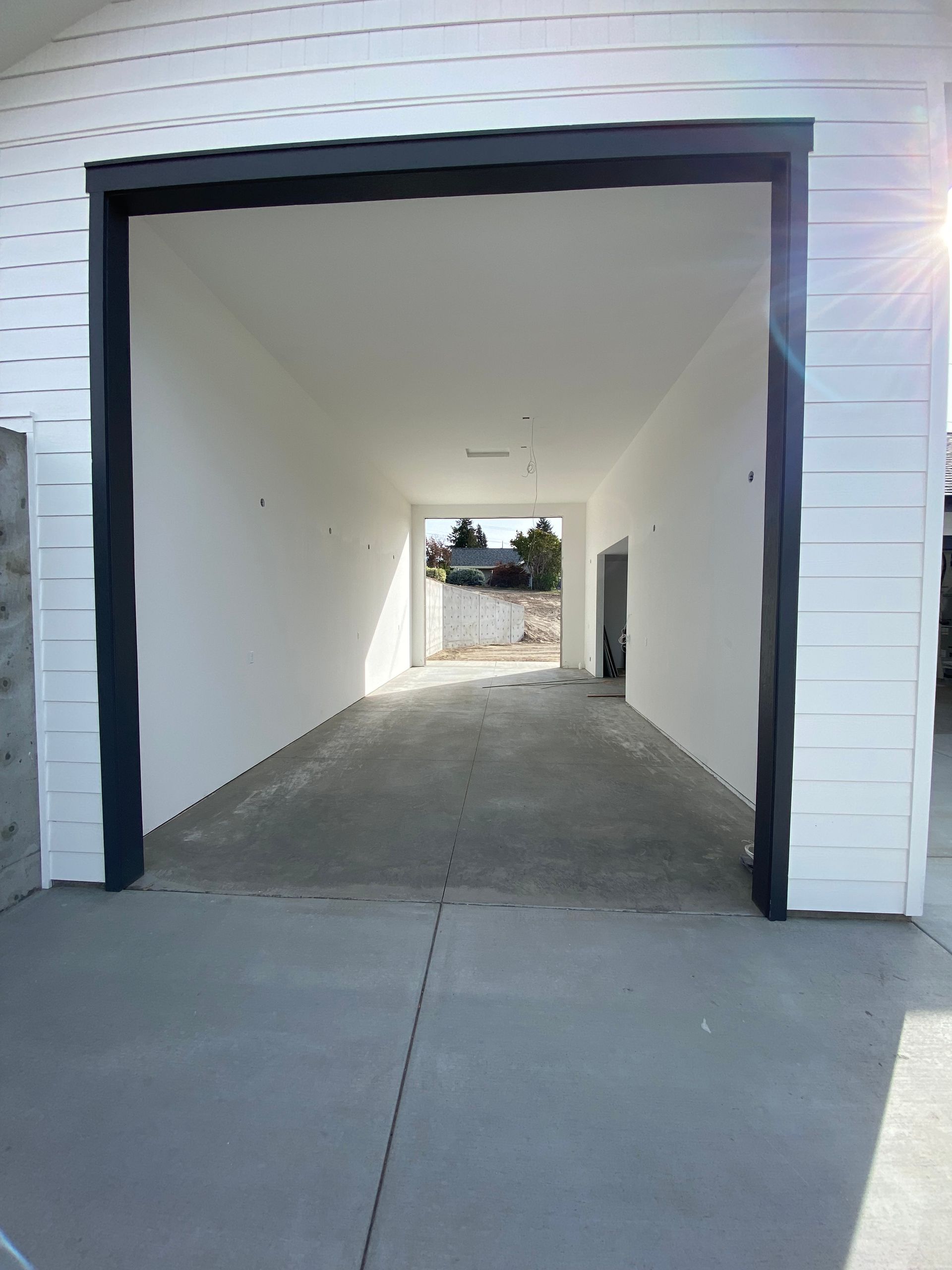 Empty white garage bay with black trim and concrete floor, open to a bright outdoor area.