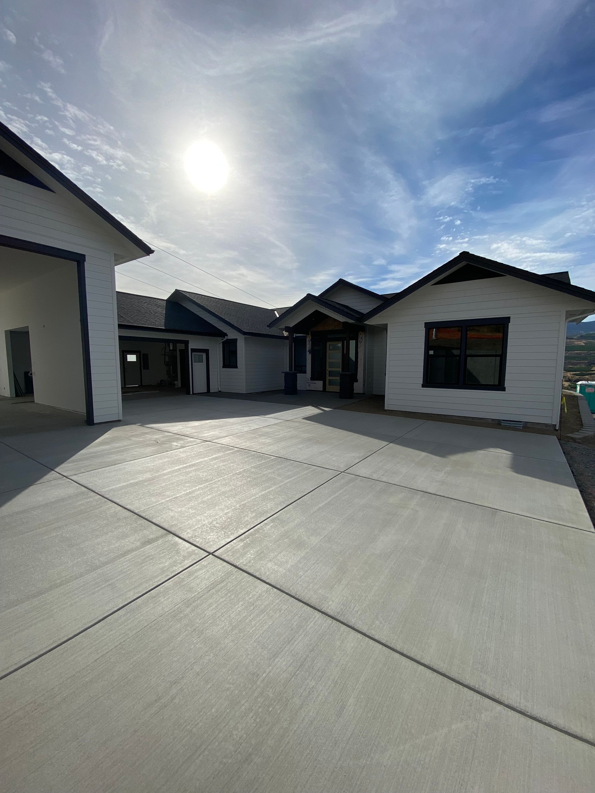 Modern residential courtyard with white houses, gray concrete, and a bright sun in a partly cloudy sky