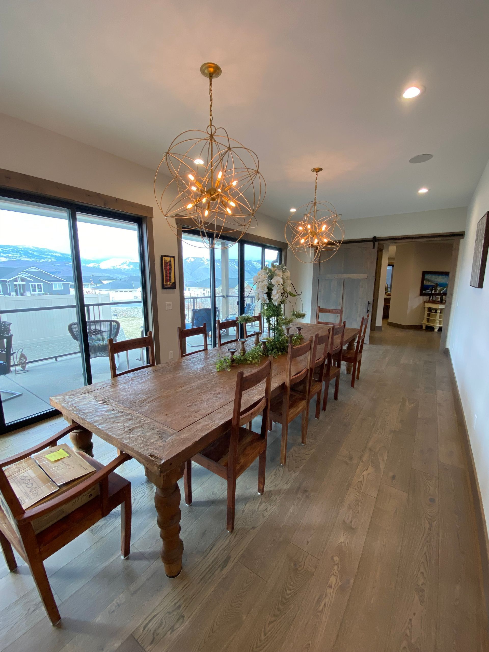 Bright dining room with long wooden table, chandeliers, large windows, and mountain view