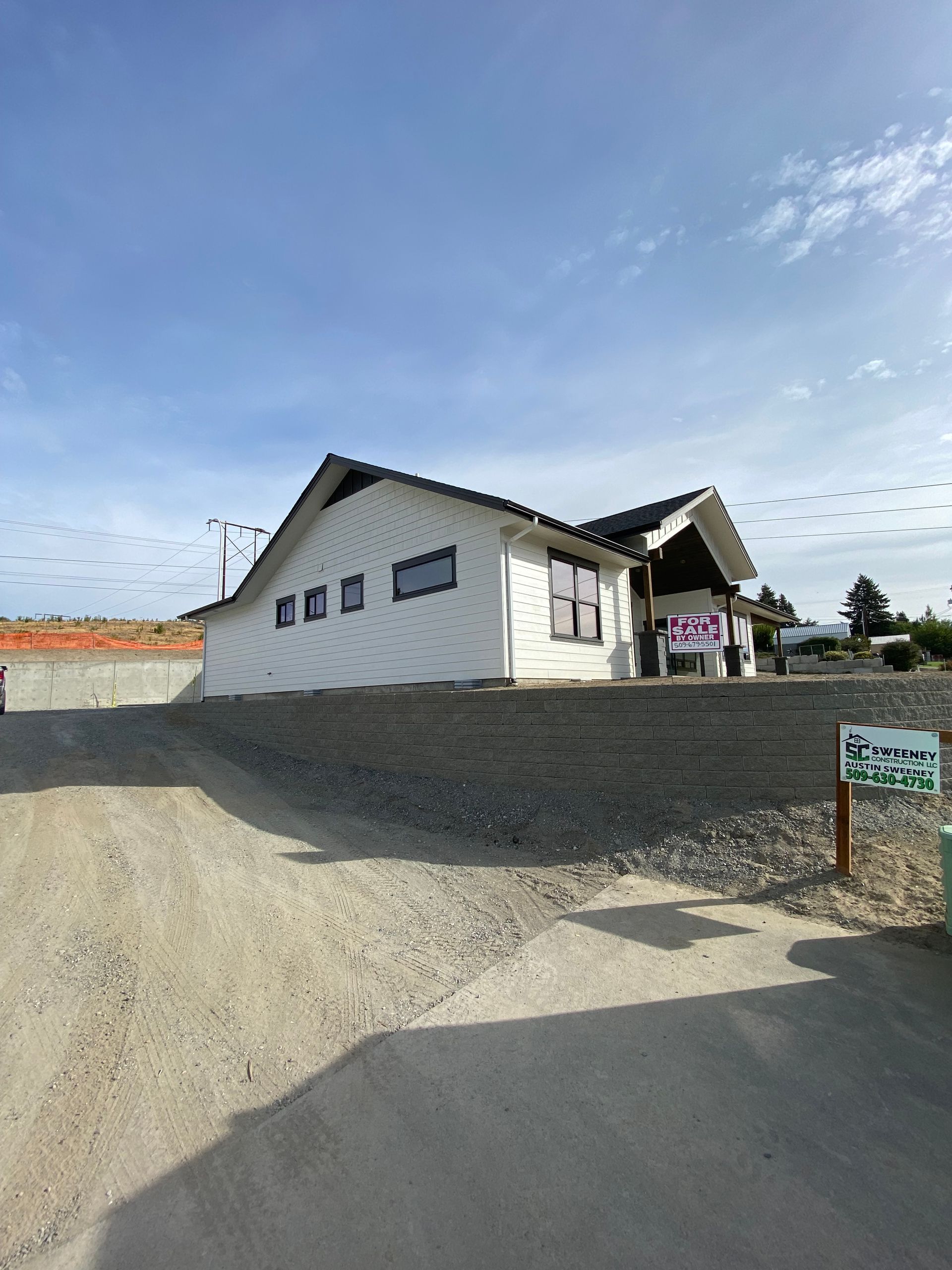 White house with a gray roof on a gravel slope under a blue sky, with a small sign in front.