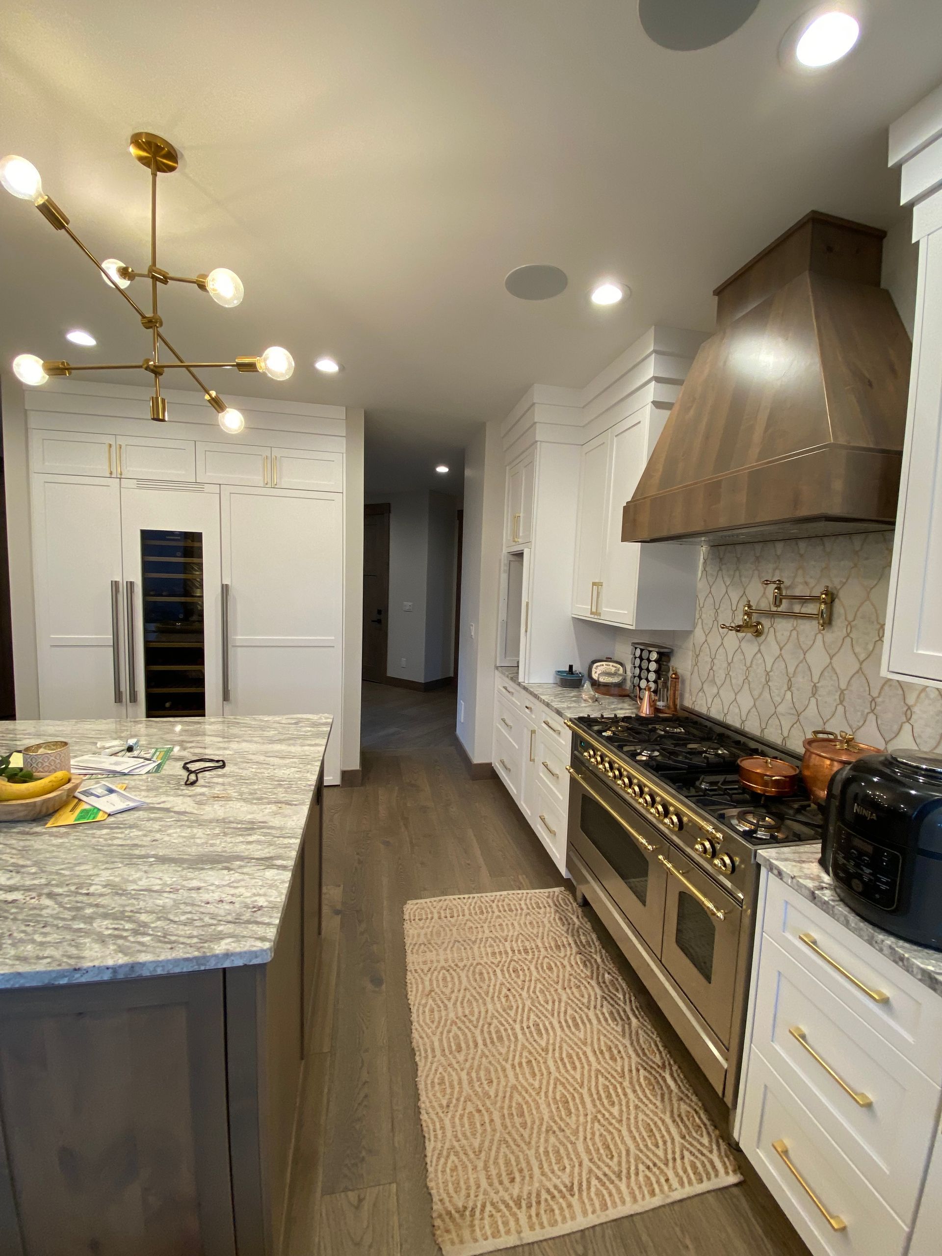 Bright modern kitchen with white cabinets, marble island, brass lights, and stainless steel stove under a hood