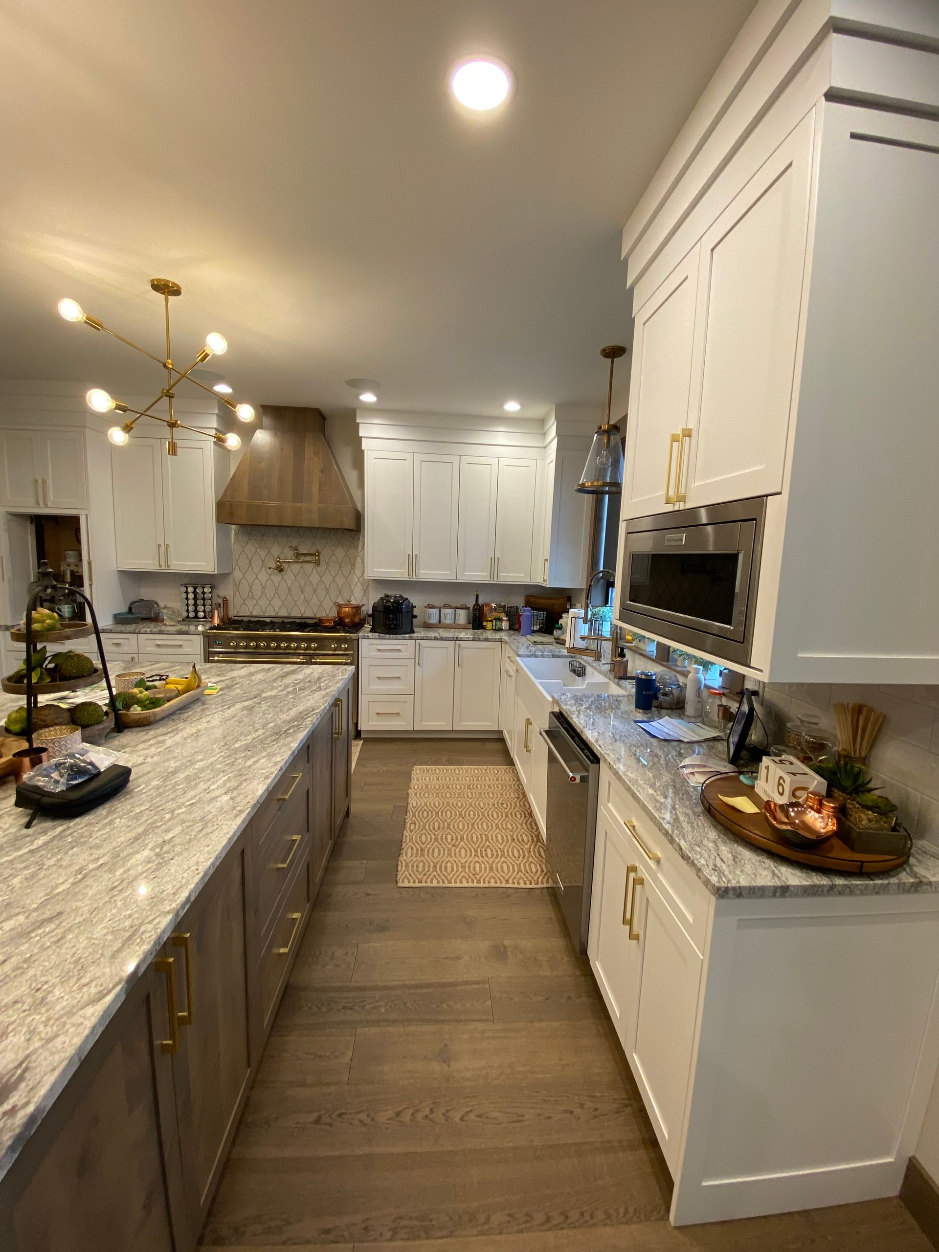 Bright white kitchen with granite island, wood floors, and warm recessed lighting