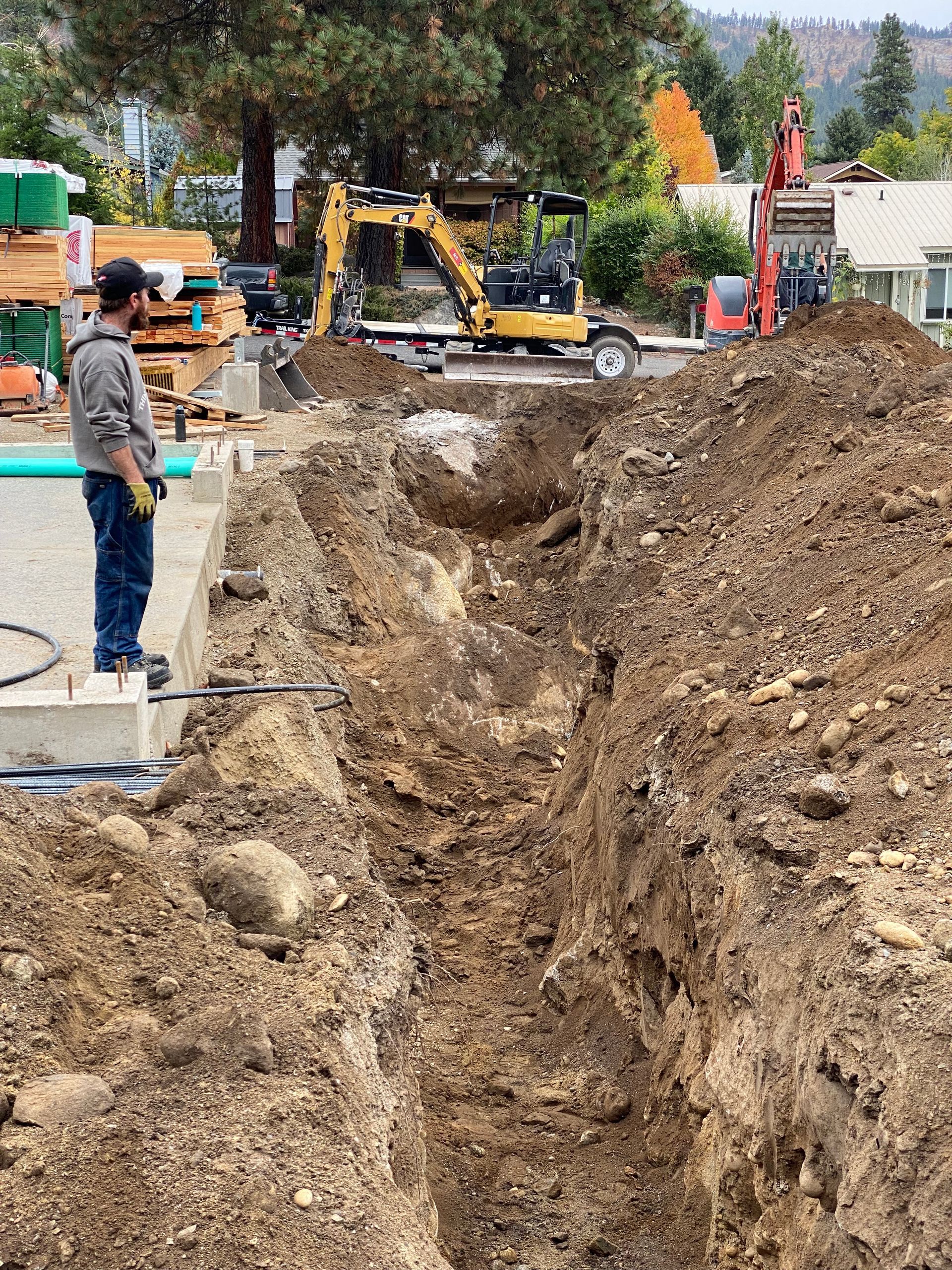 Construction site with concrete pump trucks pouring concrete into foundation forms under a blue sky.