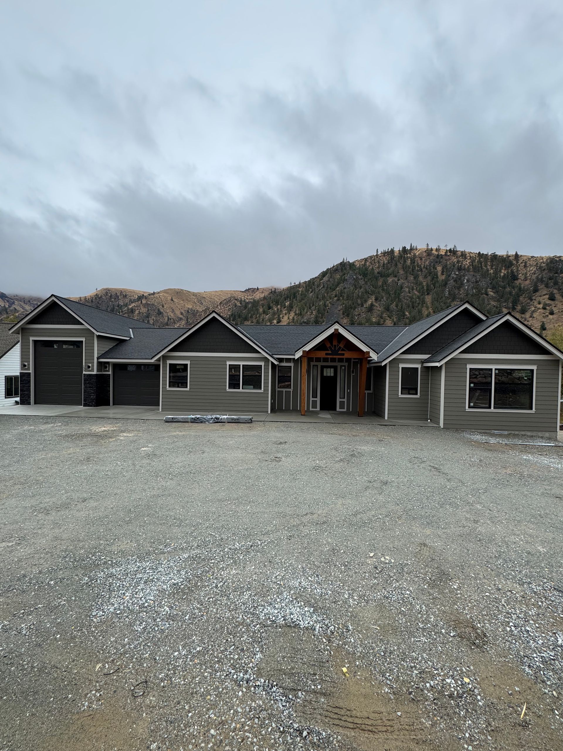 Row of gray cabins with black roofs on a gravel lot under an overcast sky