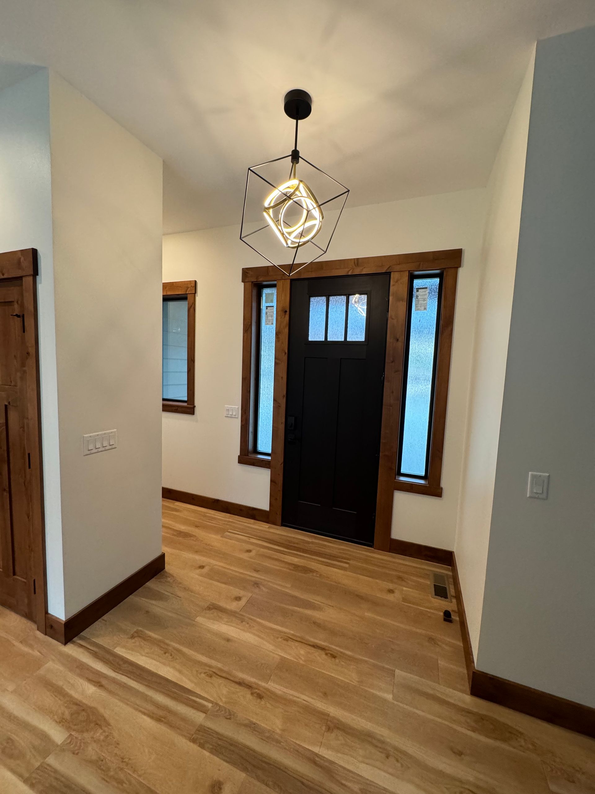 Narrow entry hall with wood floors, white walls, dark front door, and hanging light fixture