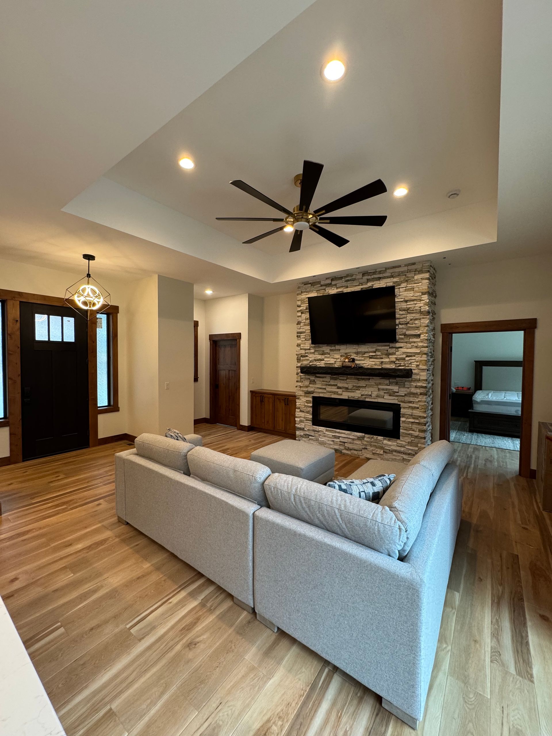 Modern living room with vaulted ceiling, gray sectional sofa, fireplace, TV, and wood flooring