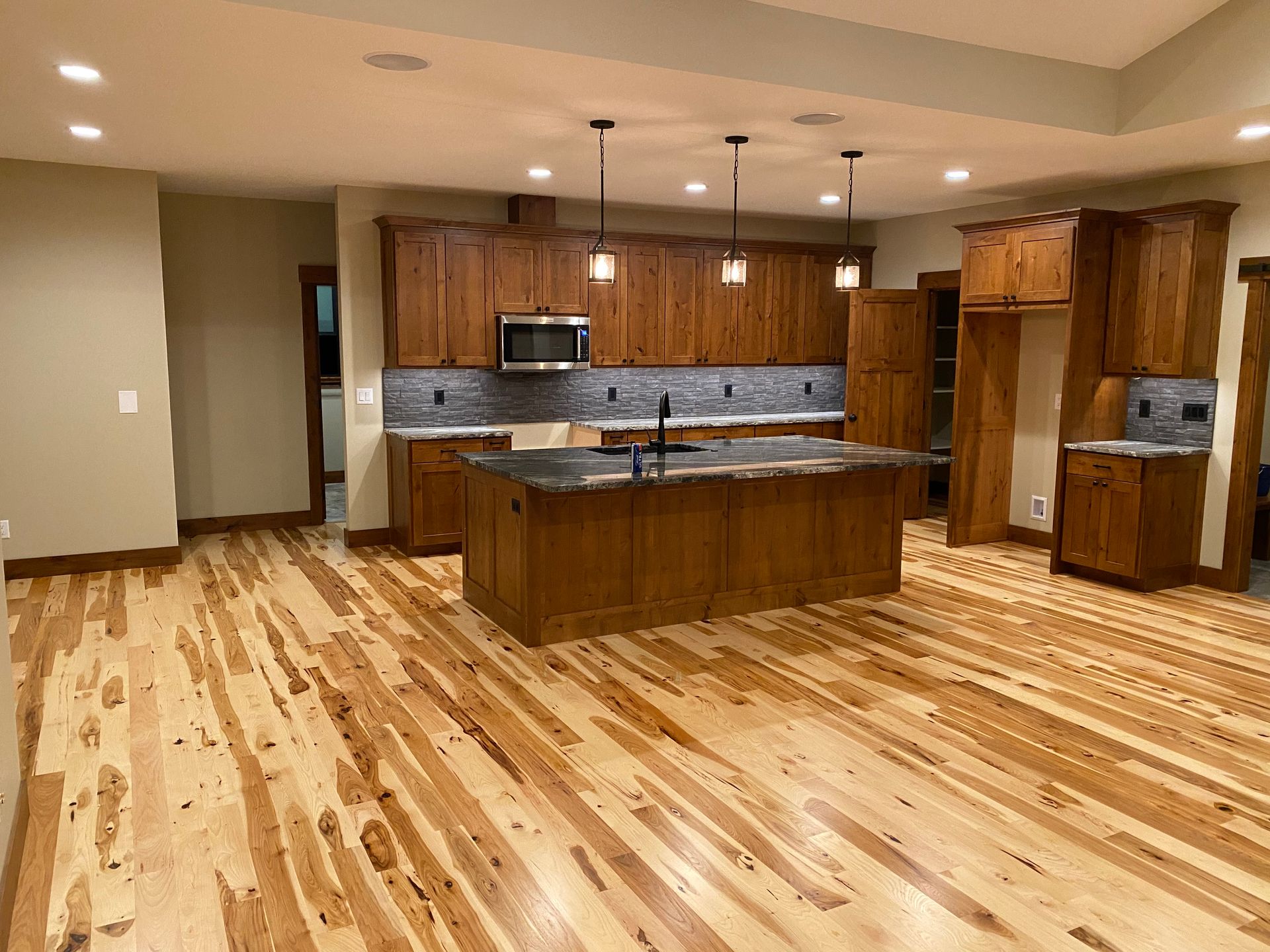 Empty modern kitchen with wood floors, brown cabinets, and a large island under pendant lights