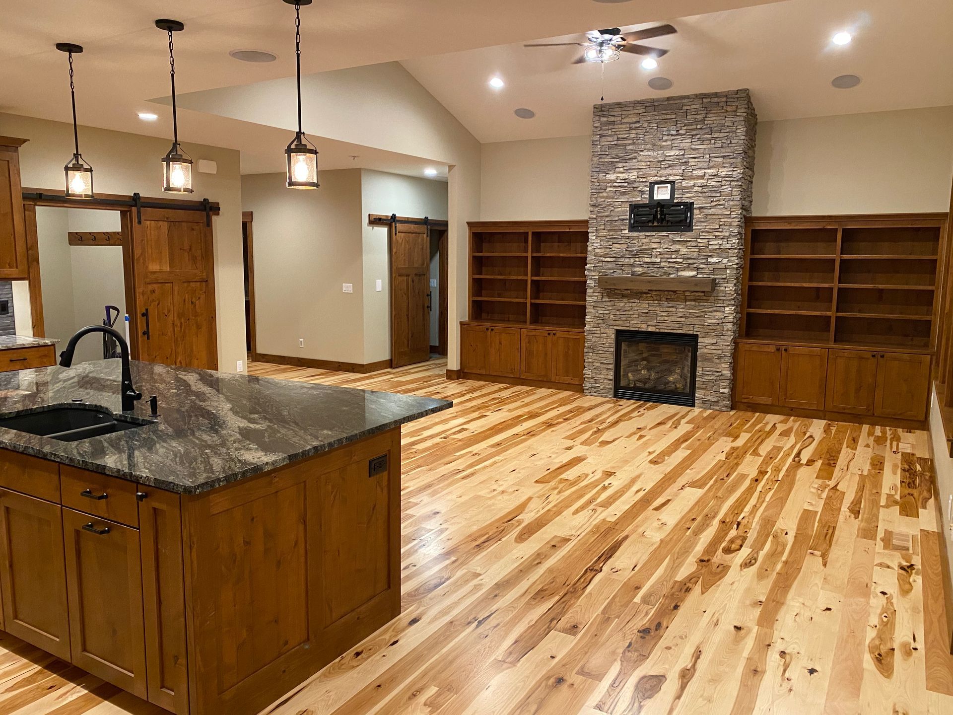 Spacious kitchen and living area with granite island, wooden floors, built-in shelves, and stone fireplace