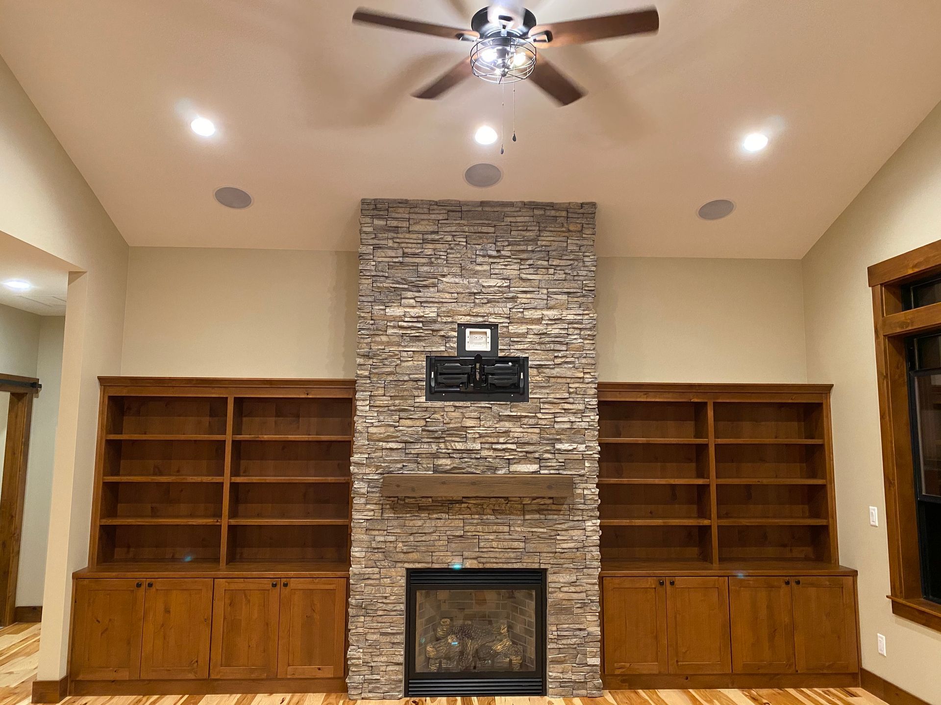 Living room with stone fireplace centered between built-in wooden shelves and cabinets, ceiling fan above