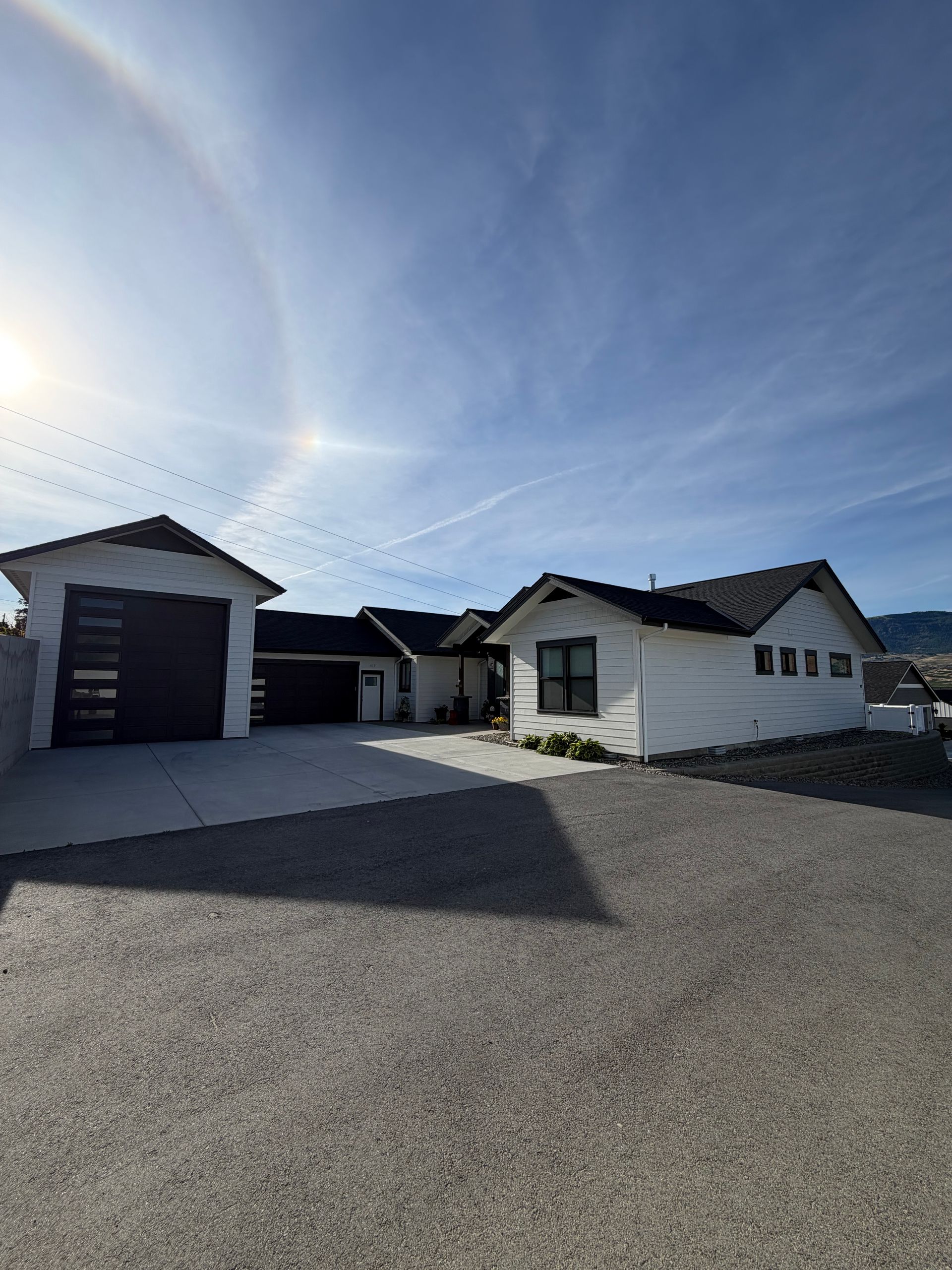 Single-story house with attached garage and paved driveway under a bright sun and blue sky.