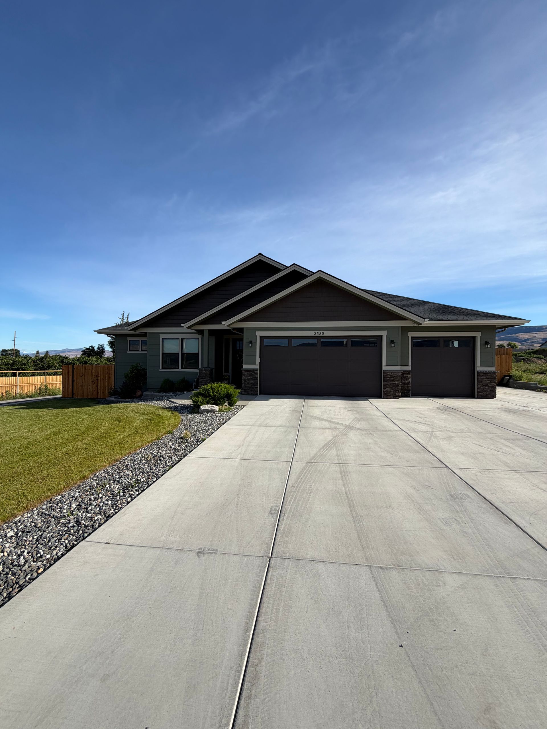 Single-story gray house with a three-car garage and long concrete driveway under a clear blue sky