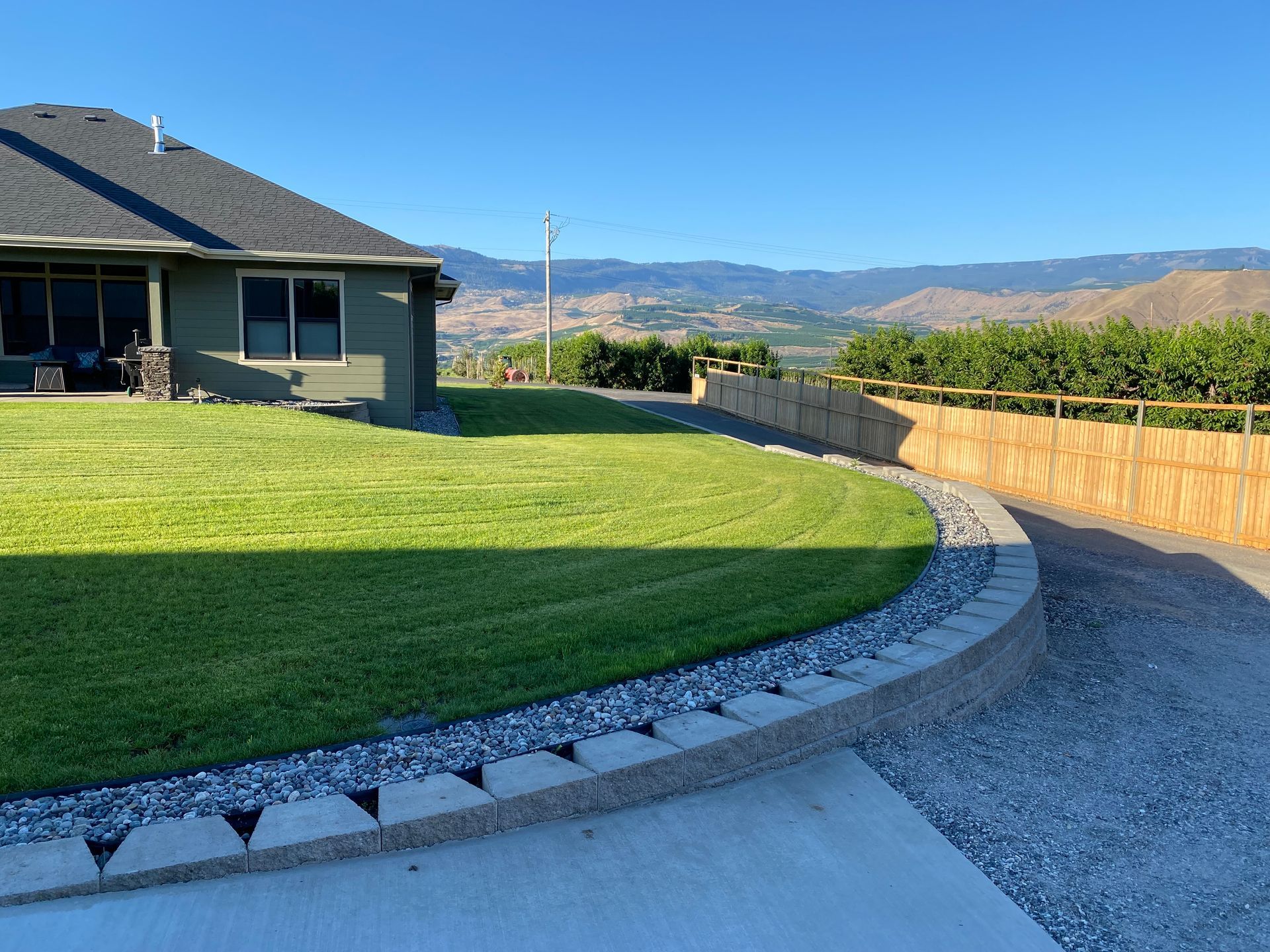 Curved stone retaining wall bordering a manicured green lawn with mountains in the background