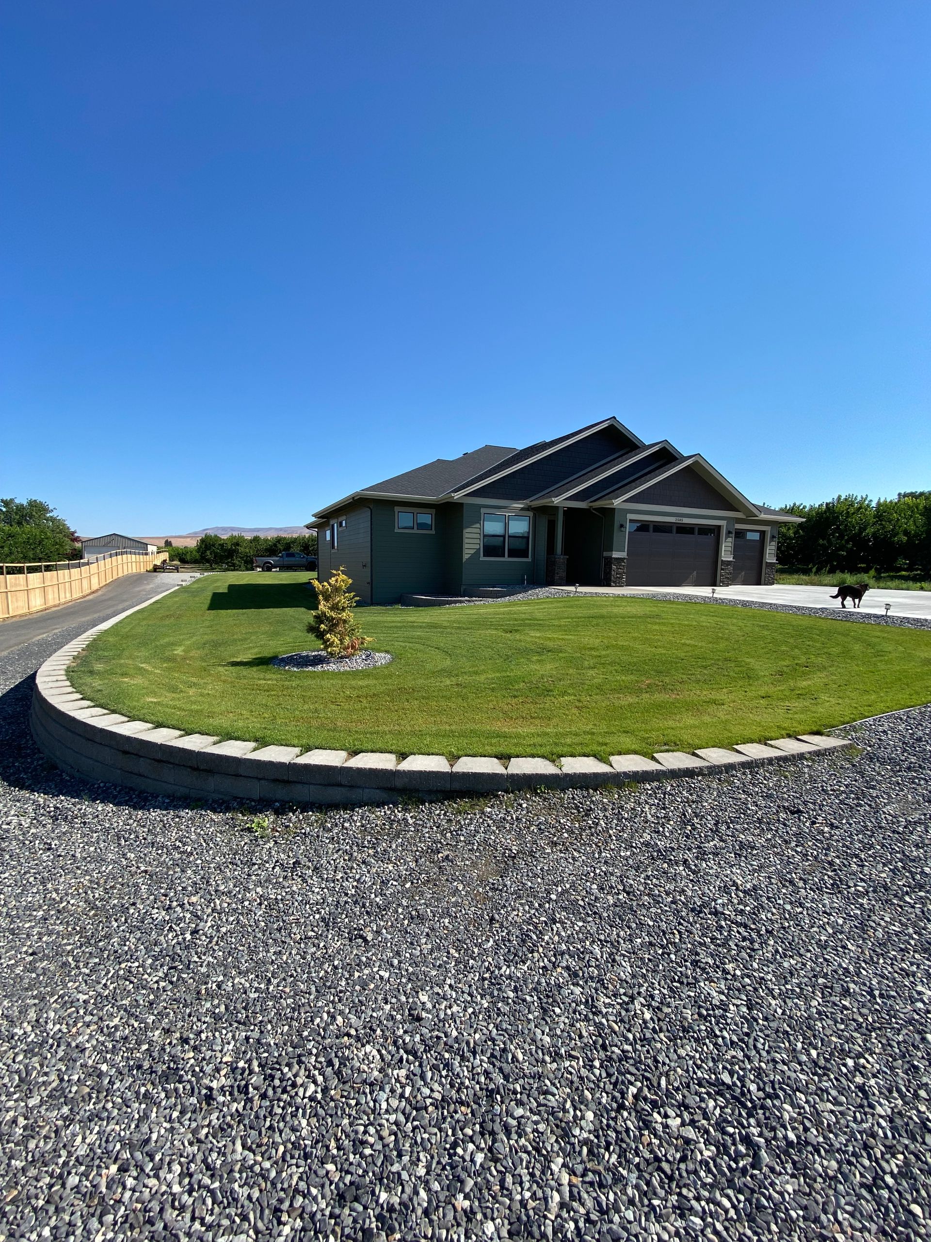 Modern gray house with a grassy yard, stone border, and gravel driveway under a clear blue sky