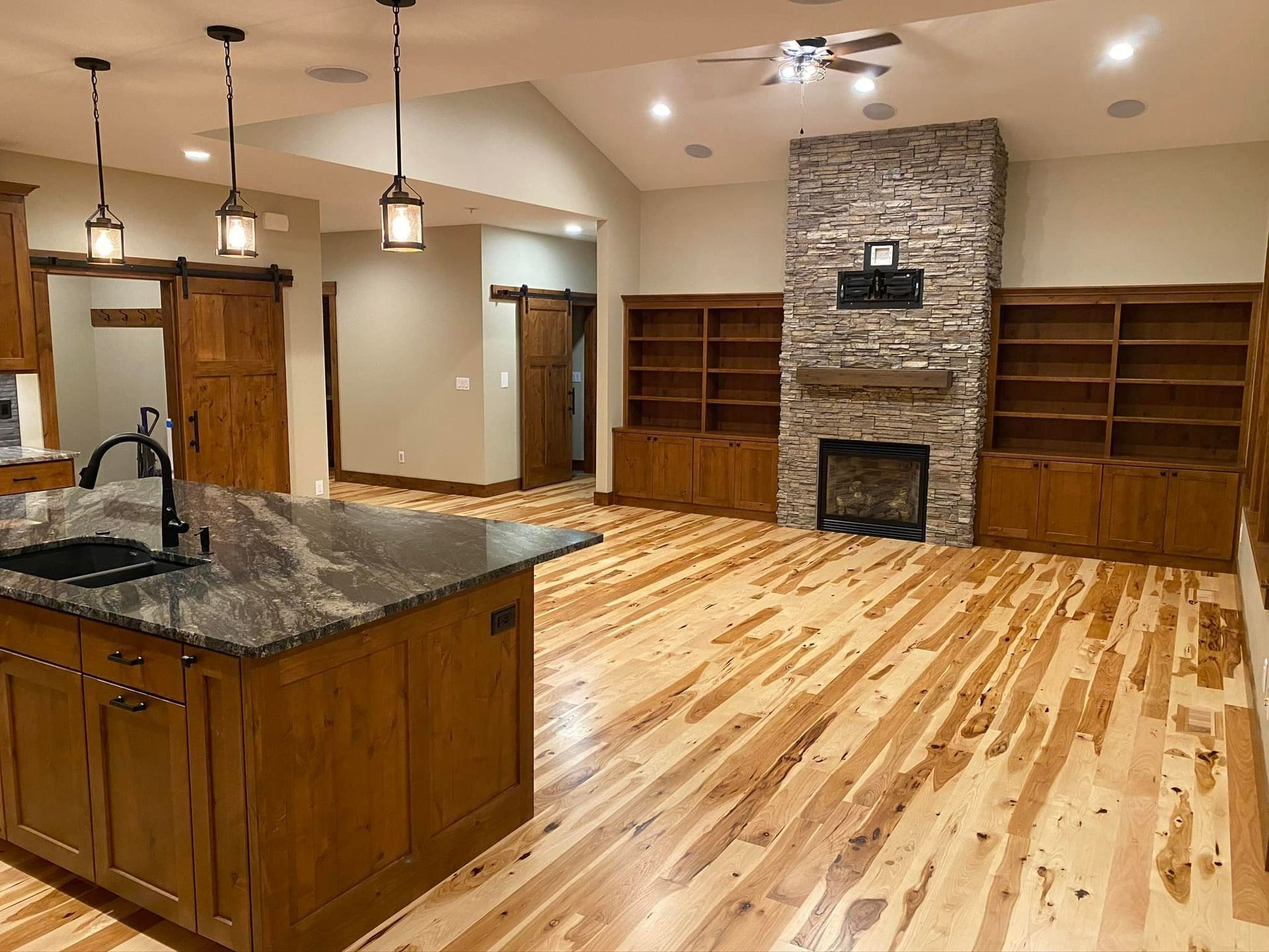 Open-concept living space with wood floors, stone fireplace, built-in shelves, and wood cabinetry.