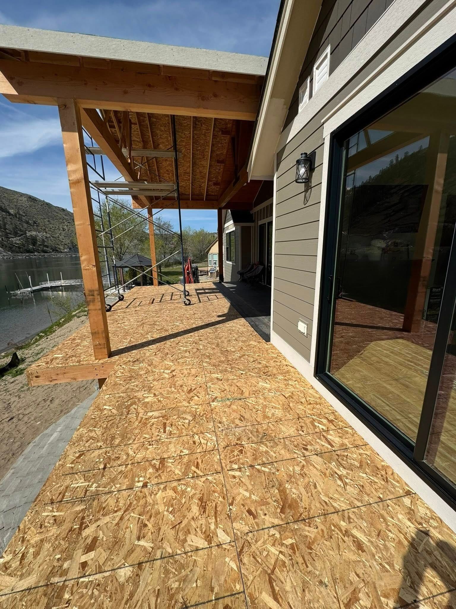 Deck under construction next to a house by water; wood boards laid out.