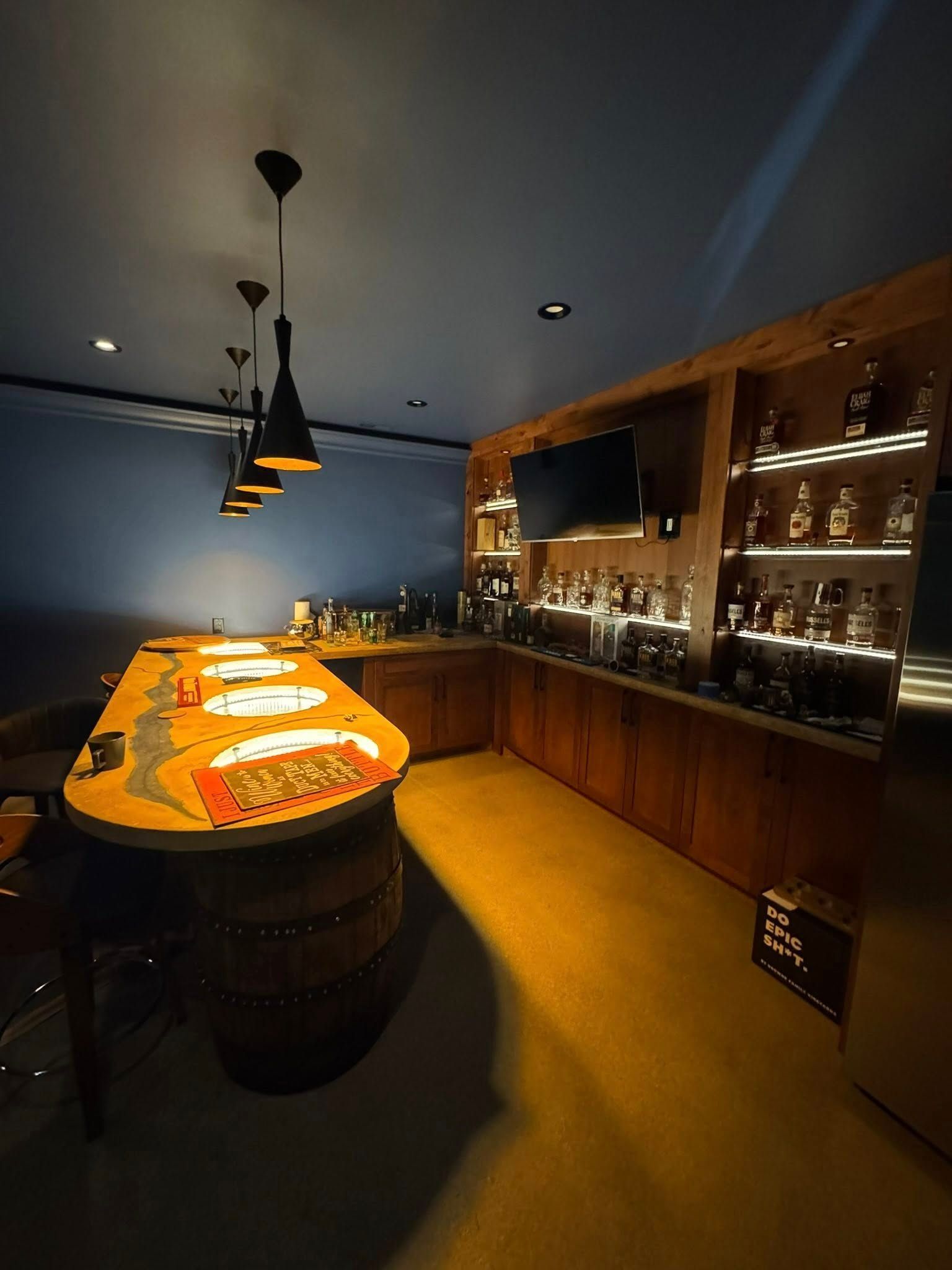 A home bar with a barrel-shaped counter and liquor shelves lit up.