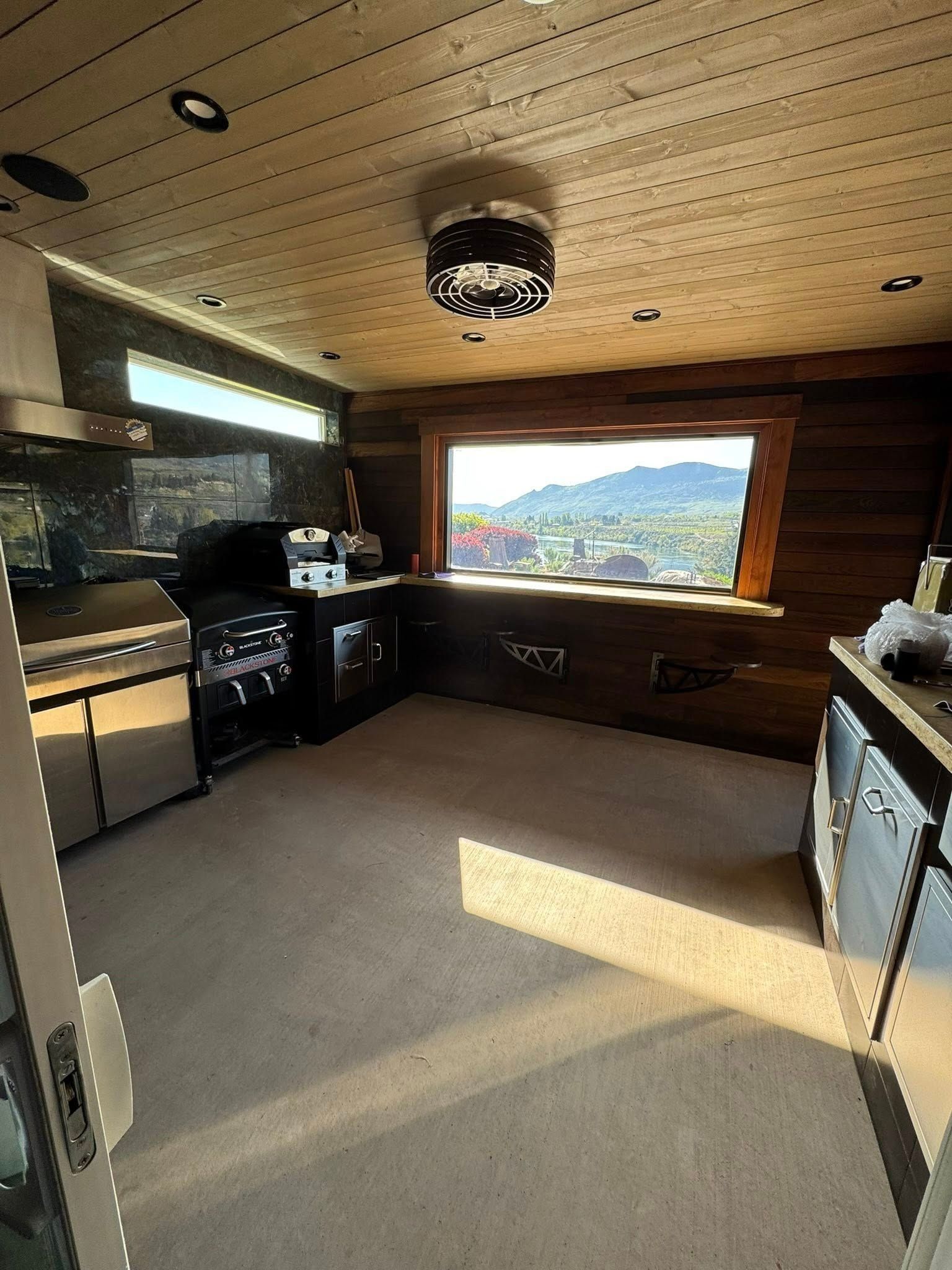 Kitchen with stainless steel appliances, dark wood paneling, a large window with a view.