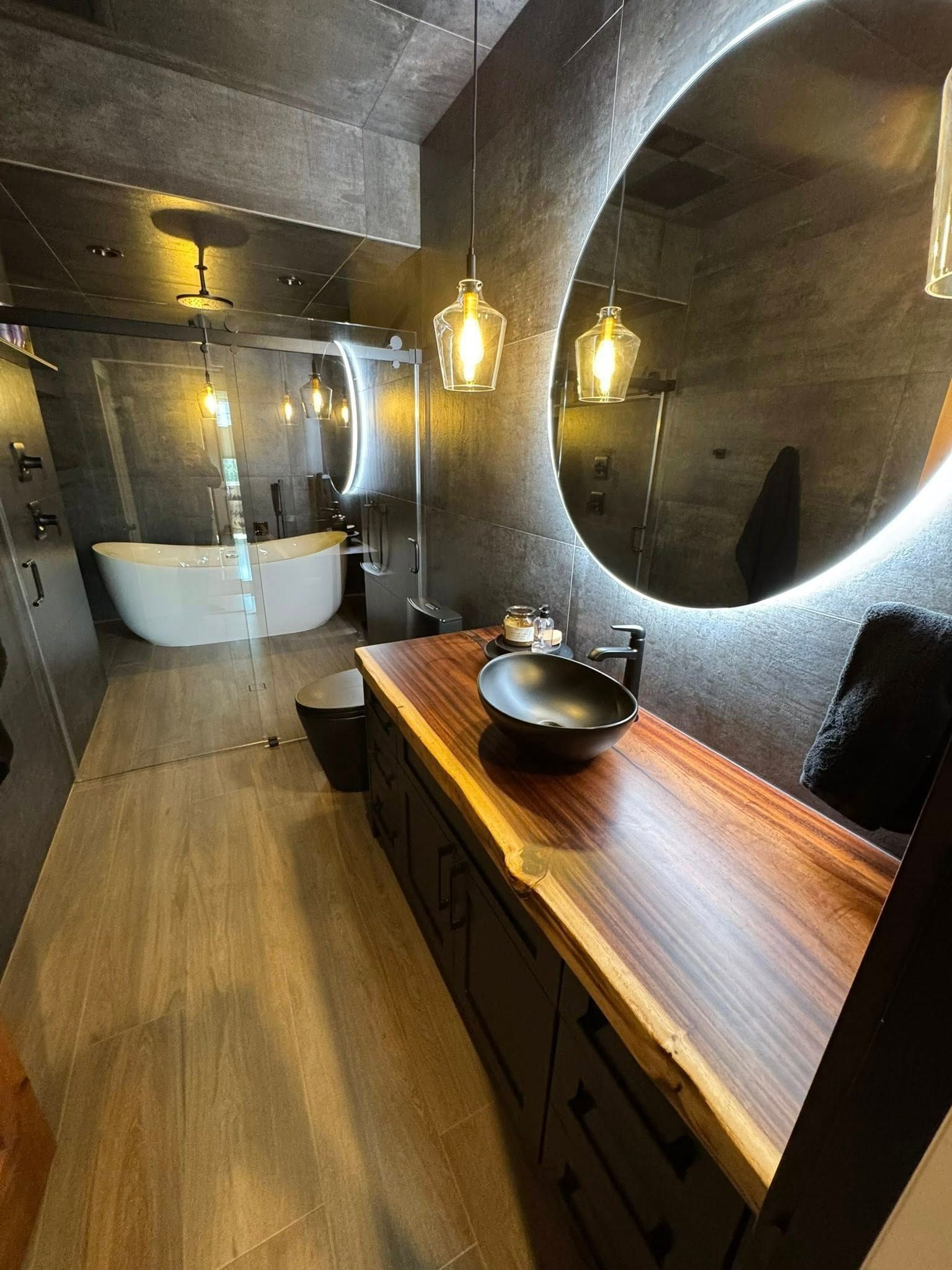 Luxurious modern bathroom with stone walls, wooden vanity, and round mirrors.
