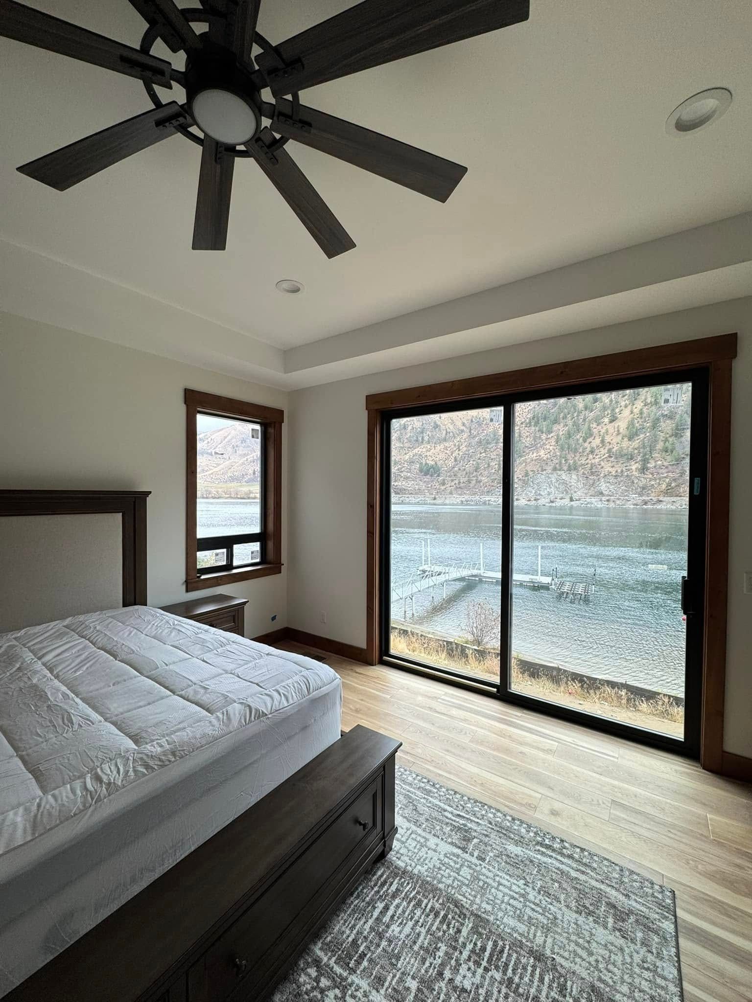 Bedroom with bed, rug, sliding glass door, and window overlooking a body of water.