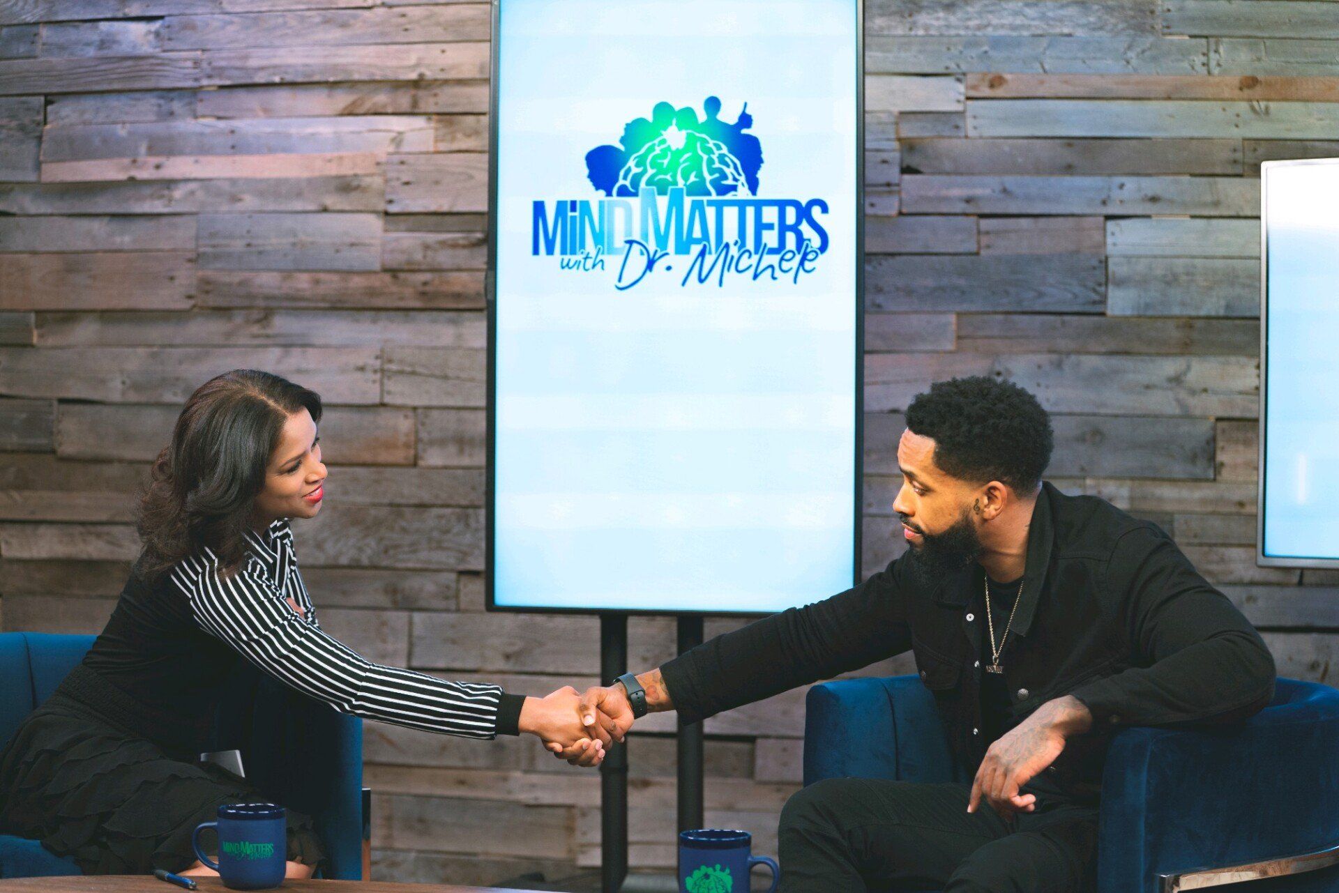 Two people shake hands on a studio set with a screen reading “Mind Matters” in the background.
