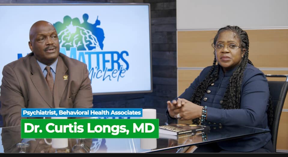 Two people seated in a studio interview, with a screen behind them and a lower-third naming Dr. Curtis Longs, MD.