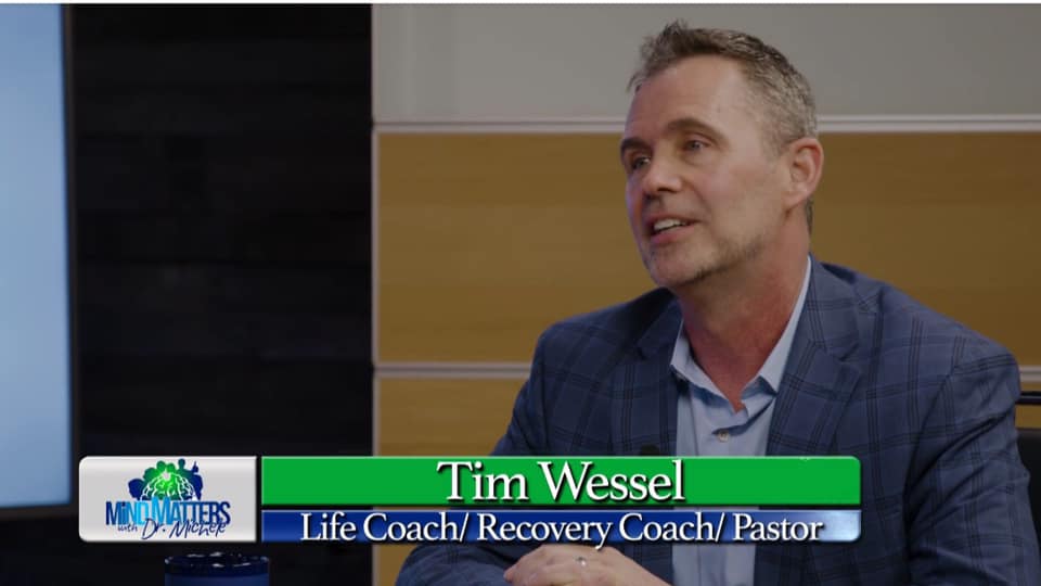 Tim Wessel speaking in a studio interview, seated beside a green lower-third name graphic.