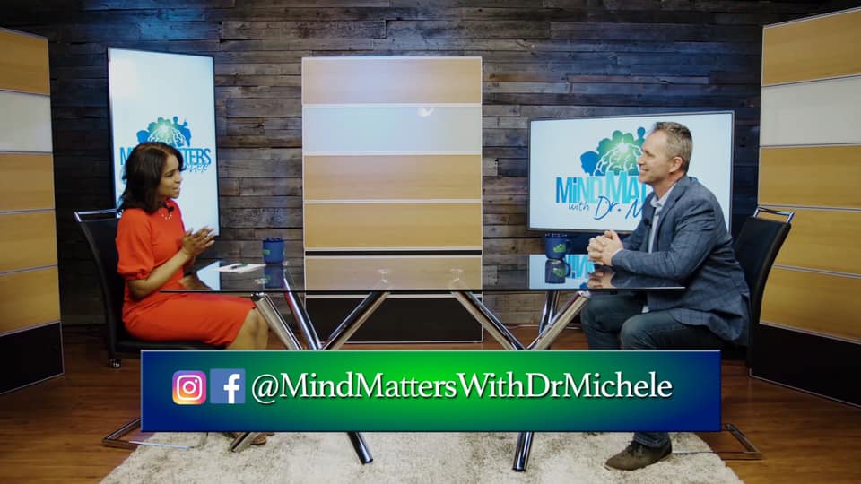 Two people talking at a studio desk with a “Mind Matters” screen and @MindMattersWithDrMichele banner.