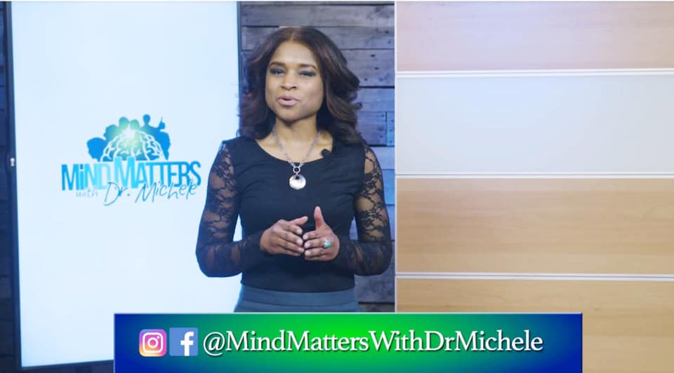 Host standing in a studio beside a “Mind Matters” logo, wearing a black dress and speaking to camera.