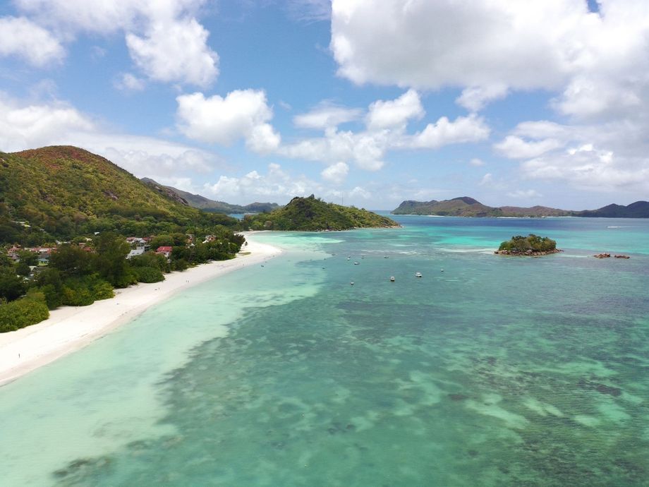 Scenic turquoise ocean and white sand beach with lush green islands under a partly cloudy sky.