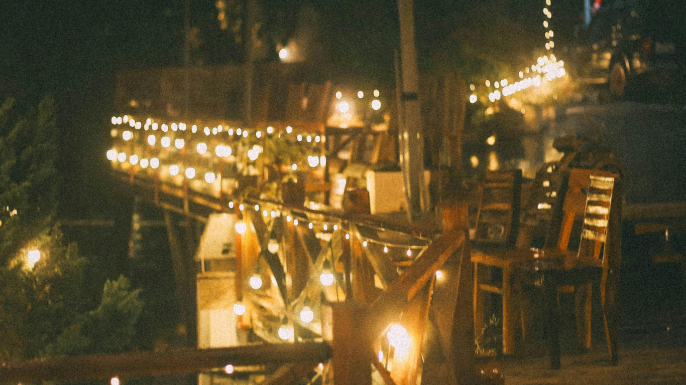Warm string lights illuminate a wooden balcony with chairs at night, creating a cozy and festive outdoor atmosphere.