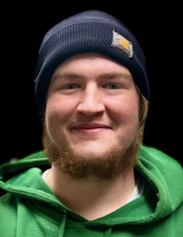 A man with a beard wearing a black beanie and a green hoodie.