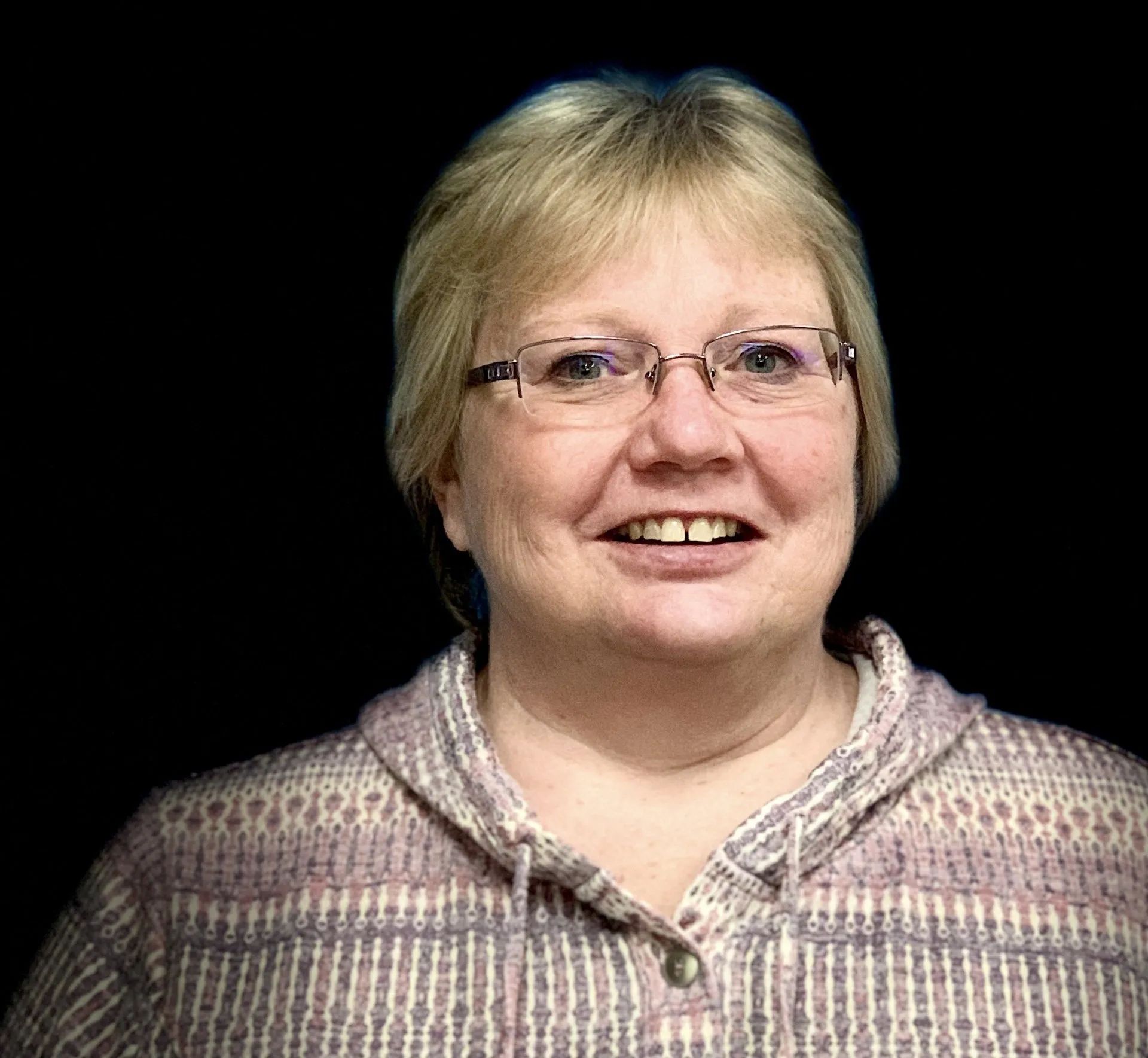 A woman wearing glasses and a sweater is smiling for the camera.