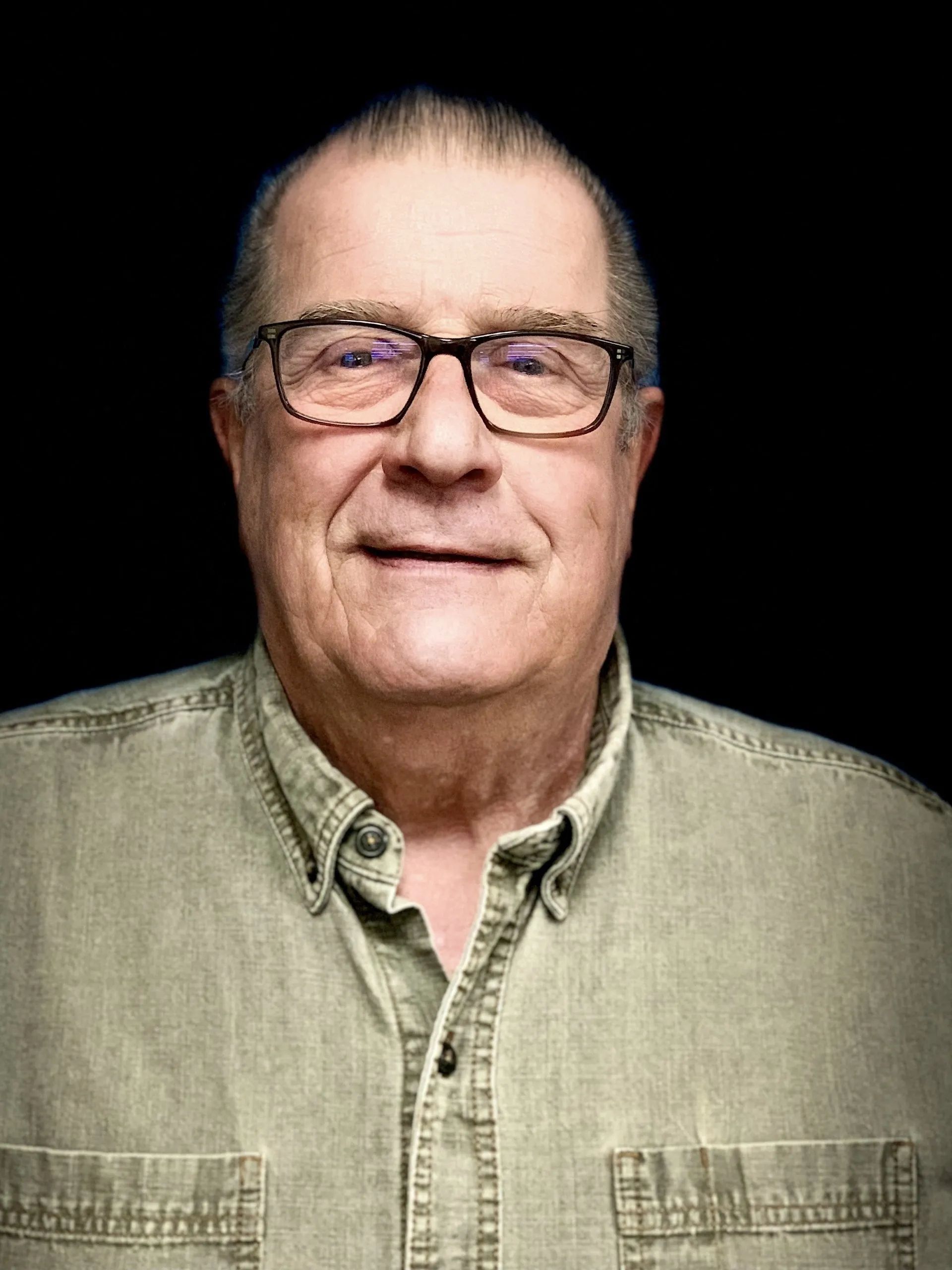 A man wearing glasses and a jacket is smiling for the camera.