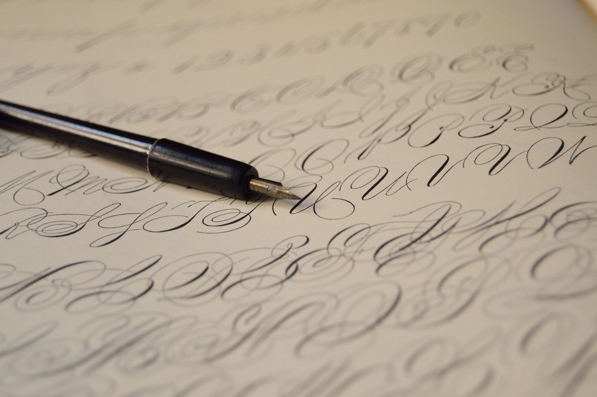 A black calligraphy pen resting on parchment paper covered in practice cursive handwriting.