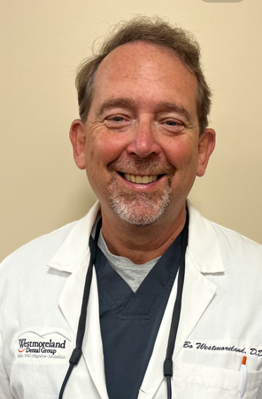 A man wearing a white lab coat and a stethoscope around his neck is smiling.