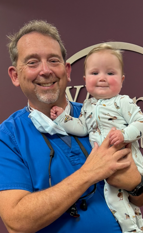 A man in a blue scrub is holding a baby in his arms.
