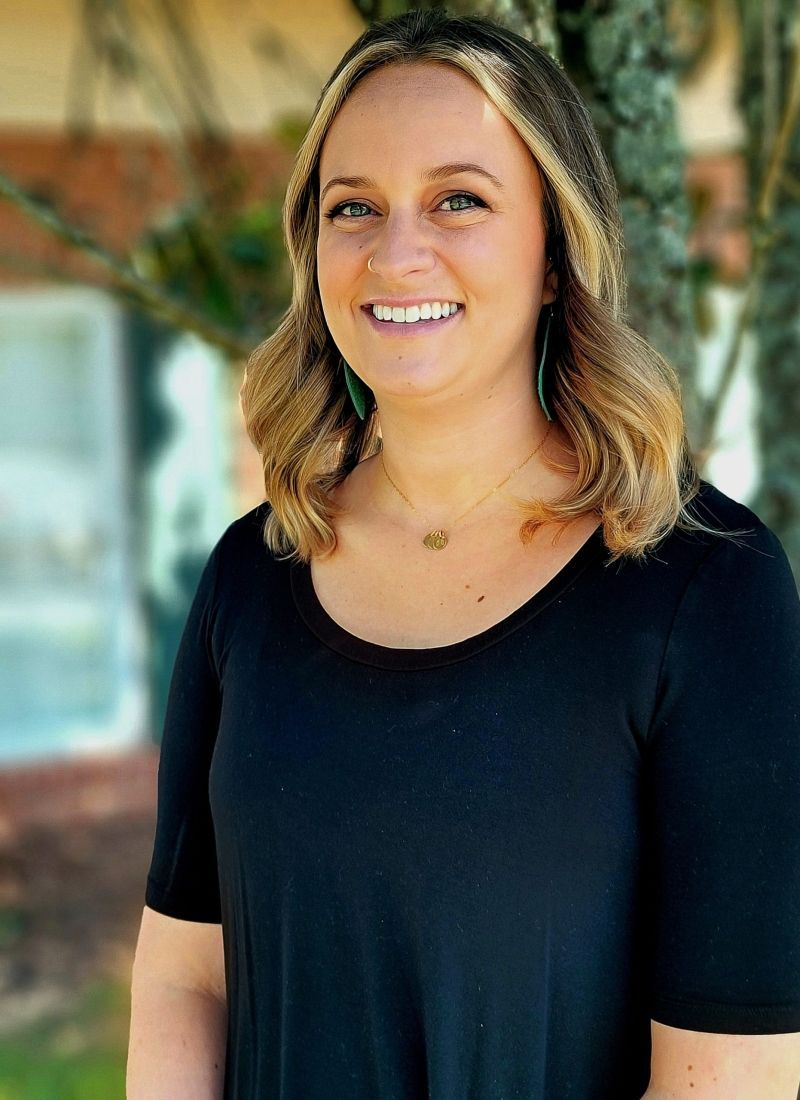 A woman in a black shirt is smiling and standing in front of a tree.