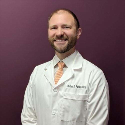 A man in a white coat and tie is smiling for the camera.