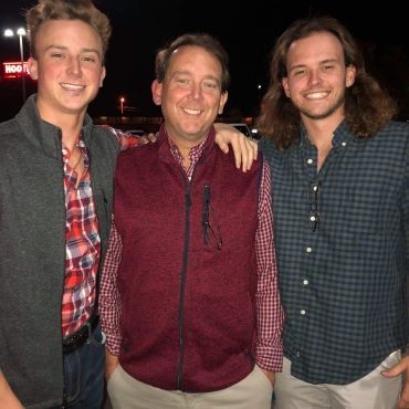 Three men posing for a picture with one wearing a maroon vest