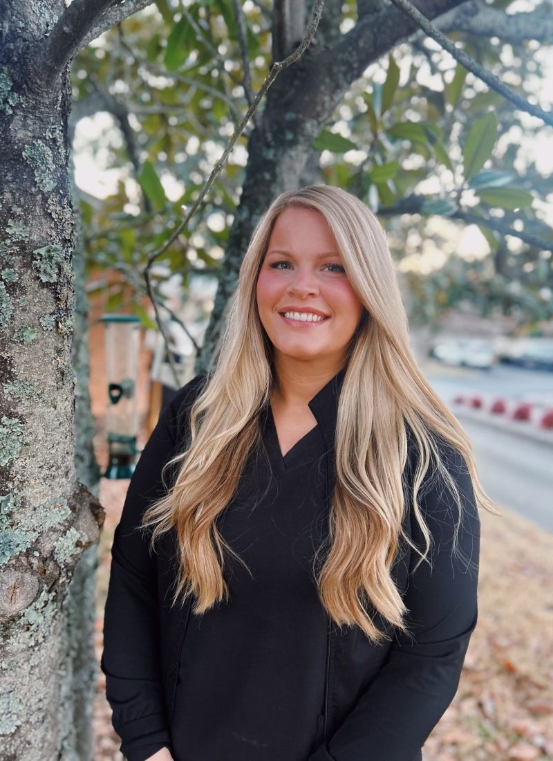 A woman in a black shirt is standing in front of a tree.