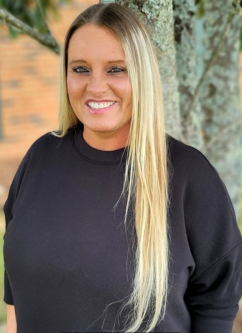 A woman in a black sweater is smiling in front of a tree.