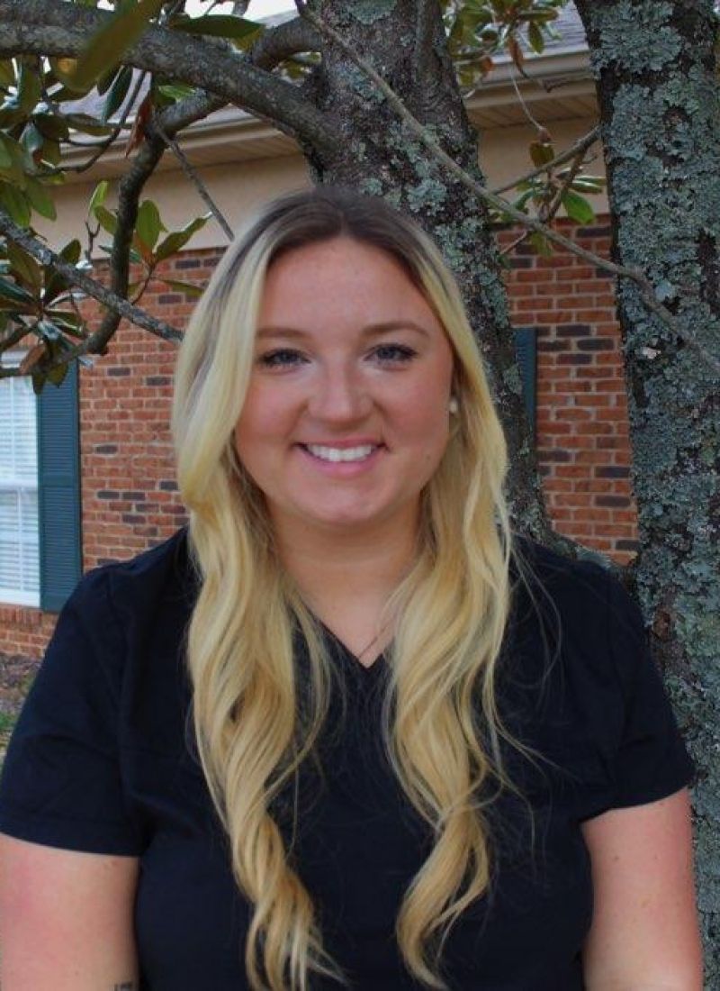 A woman in a black shirt is smiling in front of a tree.