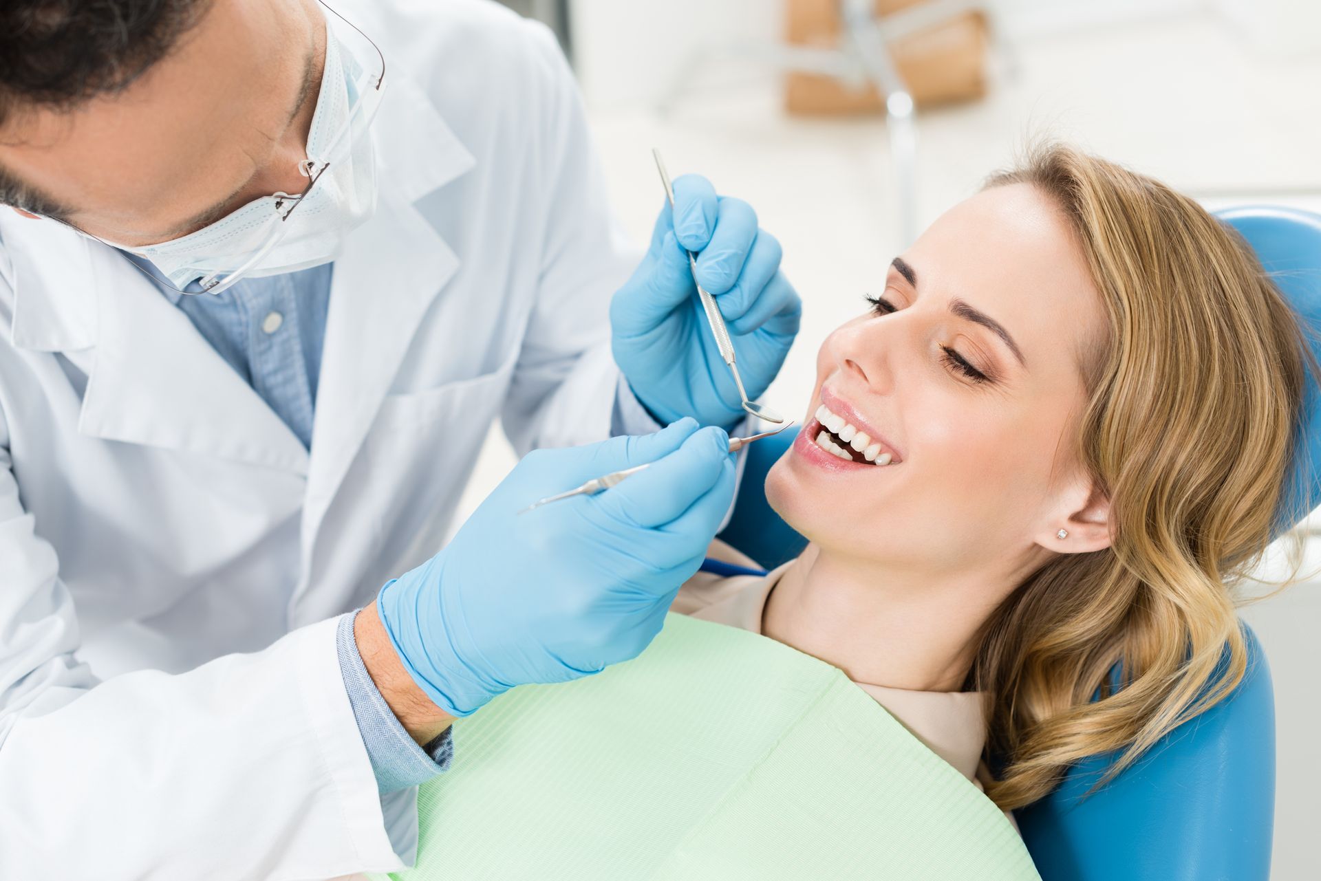 A woman is sitting in a dental chair while a dentist examines her teeth.