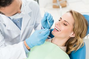 A woman is sitting in a dental chair while a dentist examines her teeth.