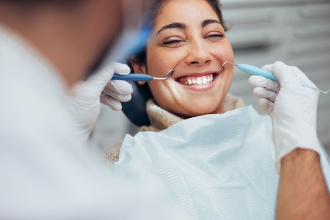 A woman is smiling while having her teeth examined by a dentist.