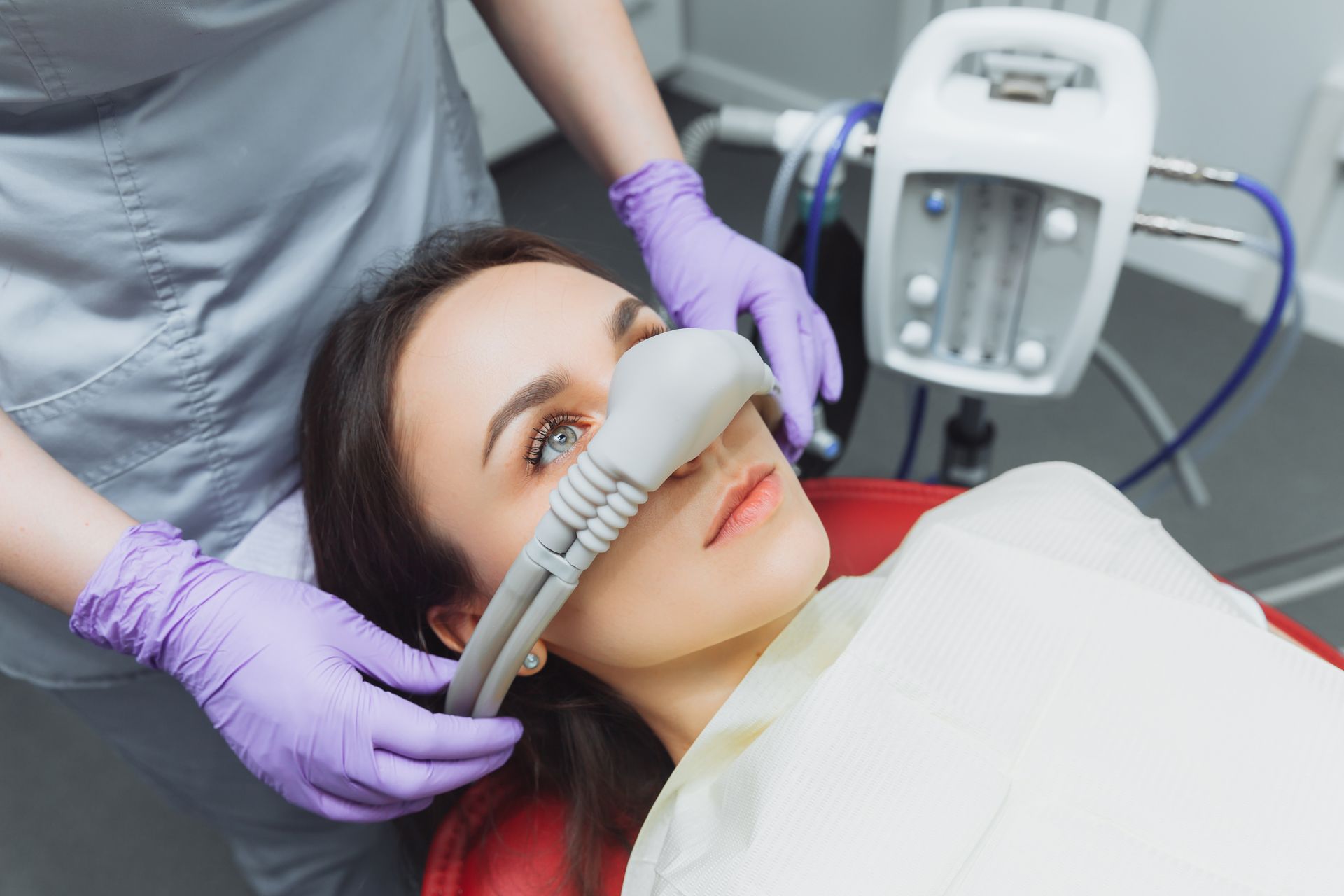 A woman is laying in a dental chair with an oxygen mask on her face.