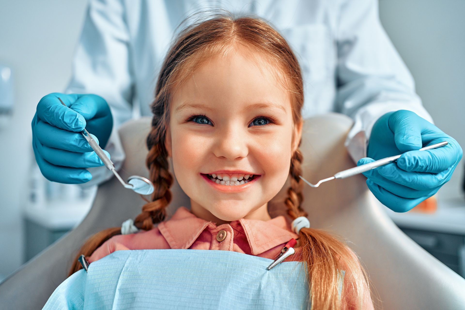 A little girl is sitting in a dental chair while a dentist examines her teeth.